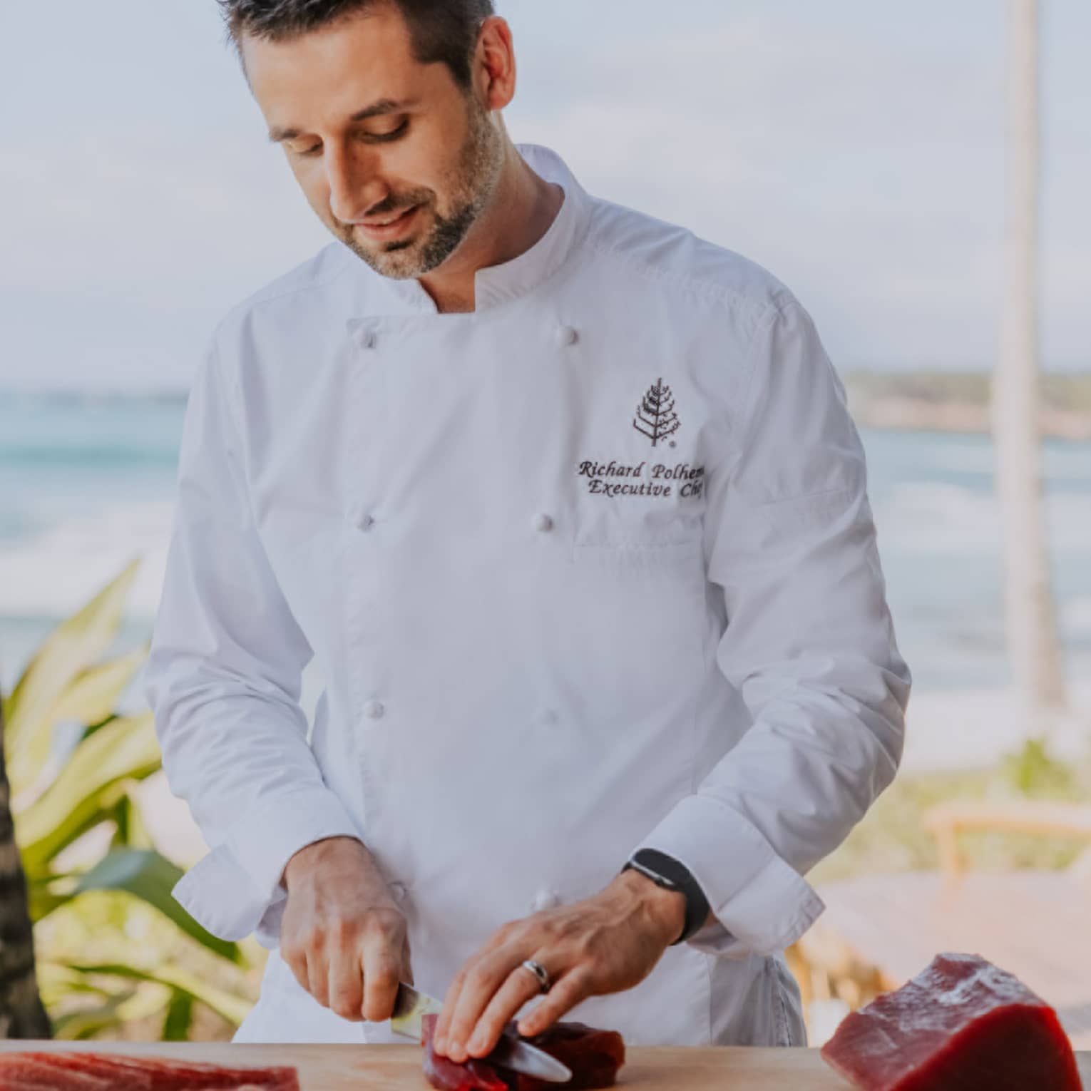 Male chef slices raw tuna on cutting board, beach in background