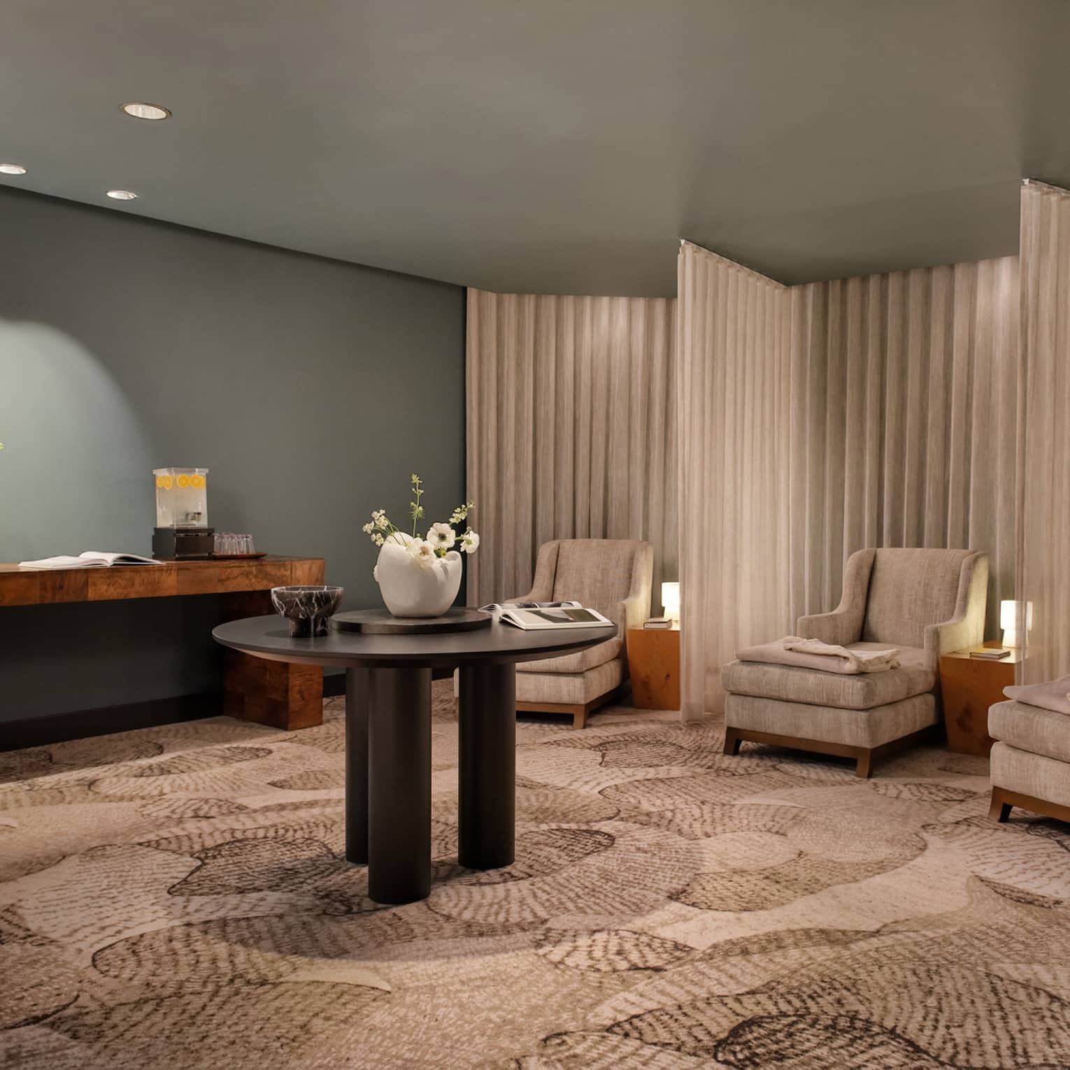 Spa relaxation area with tan armchairs separated by curtains, round table in middle of room with vase of flowers