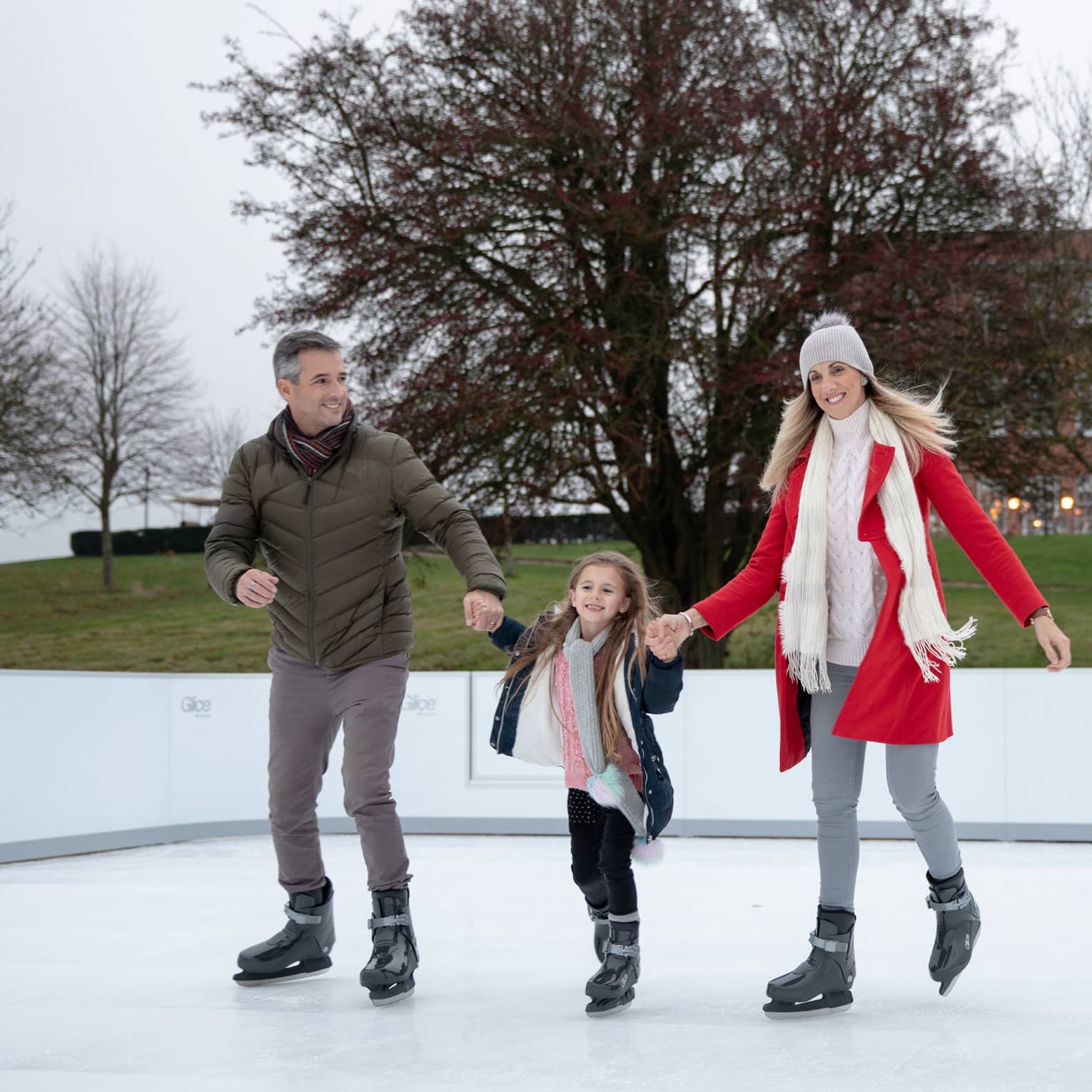 Man and woman holding hands of young girl while ice skating on outdoor rink