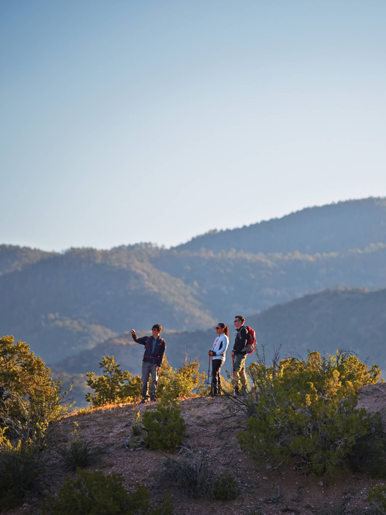 Three people hike on desert mountain hill