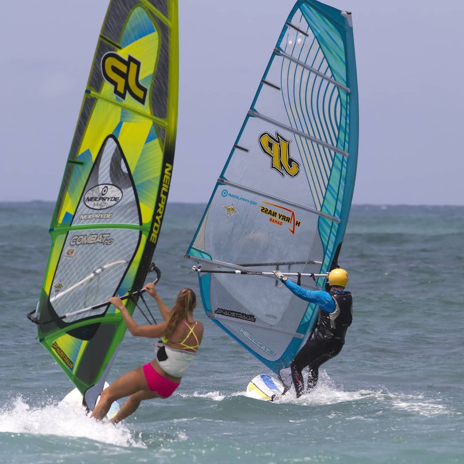 Two windsurfers leaning into the open sea under an azure blue sky, each creating a small wake.