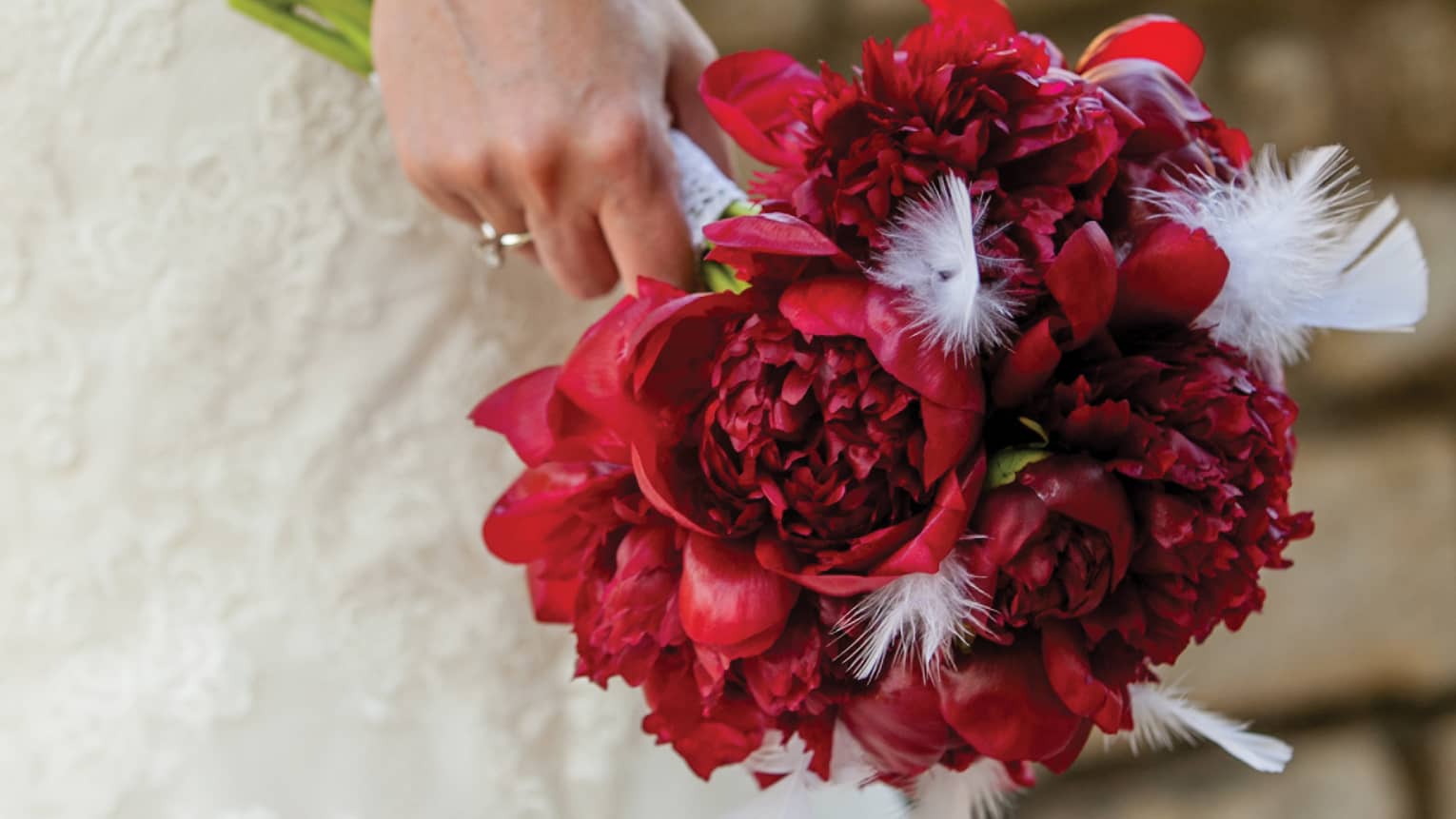 Bride wearing white wedding gown holding bouquet of red flowers 