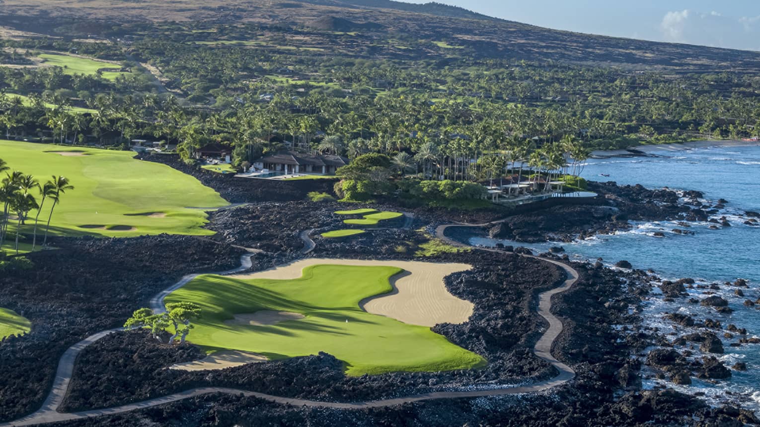 A lush green golf course lined with black lava, verdant forest, and azure ocean views