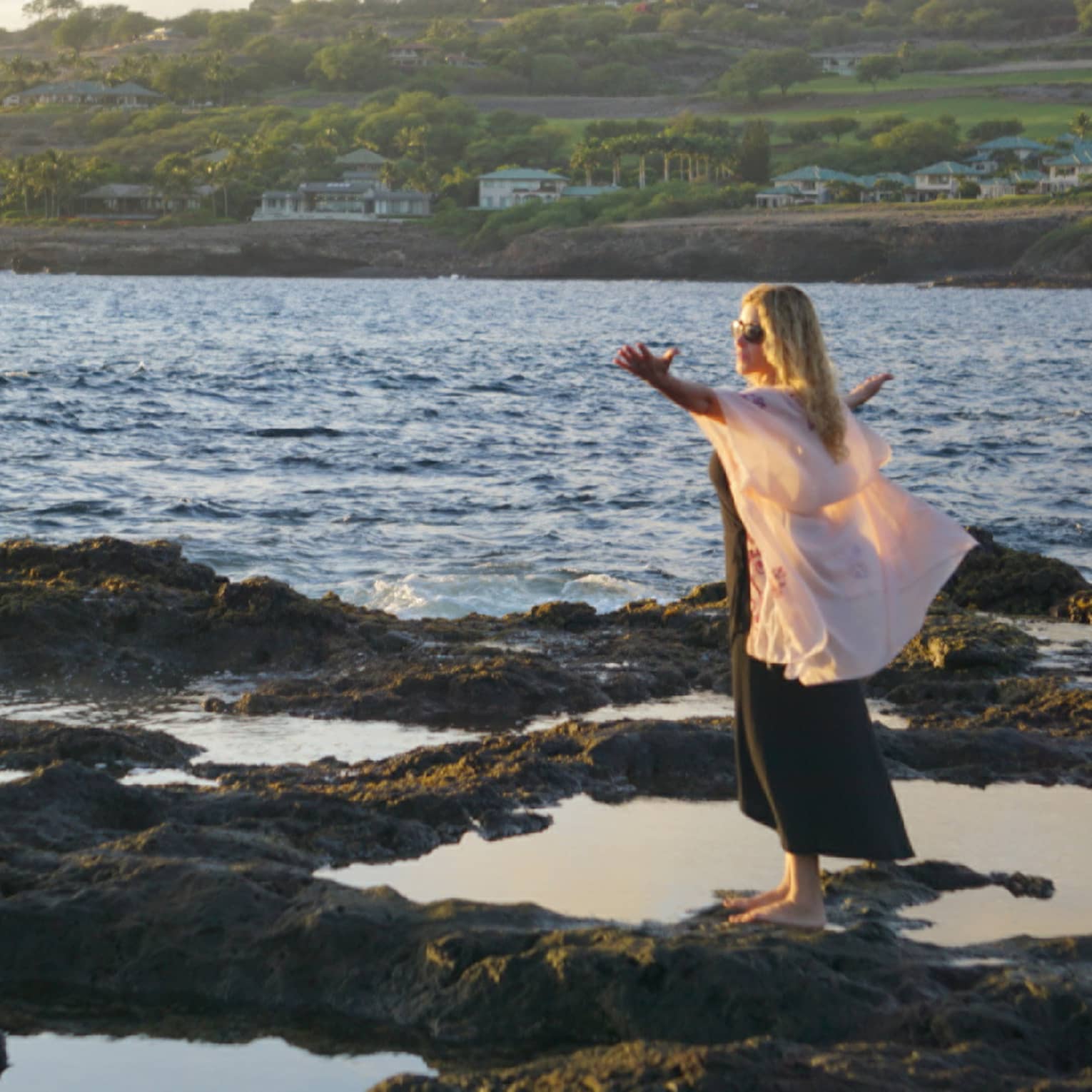 A woman meditates at edge of ocean on lava rock