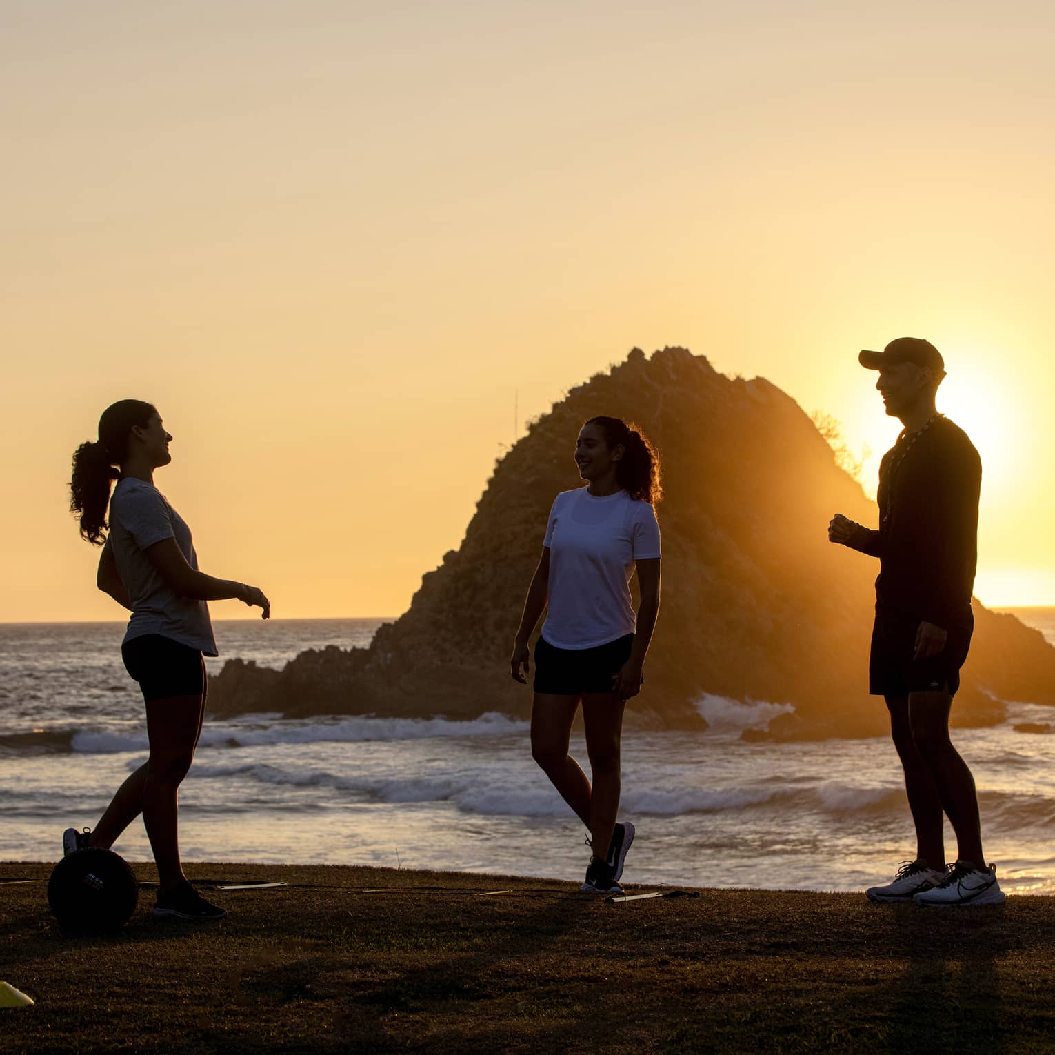 Four people standing on a beach at sunset