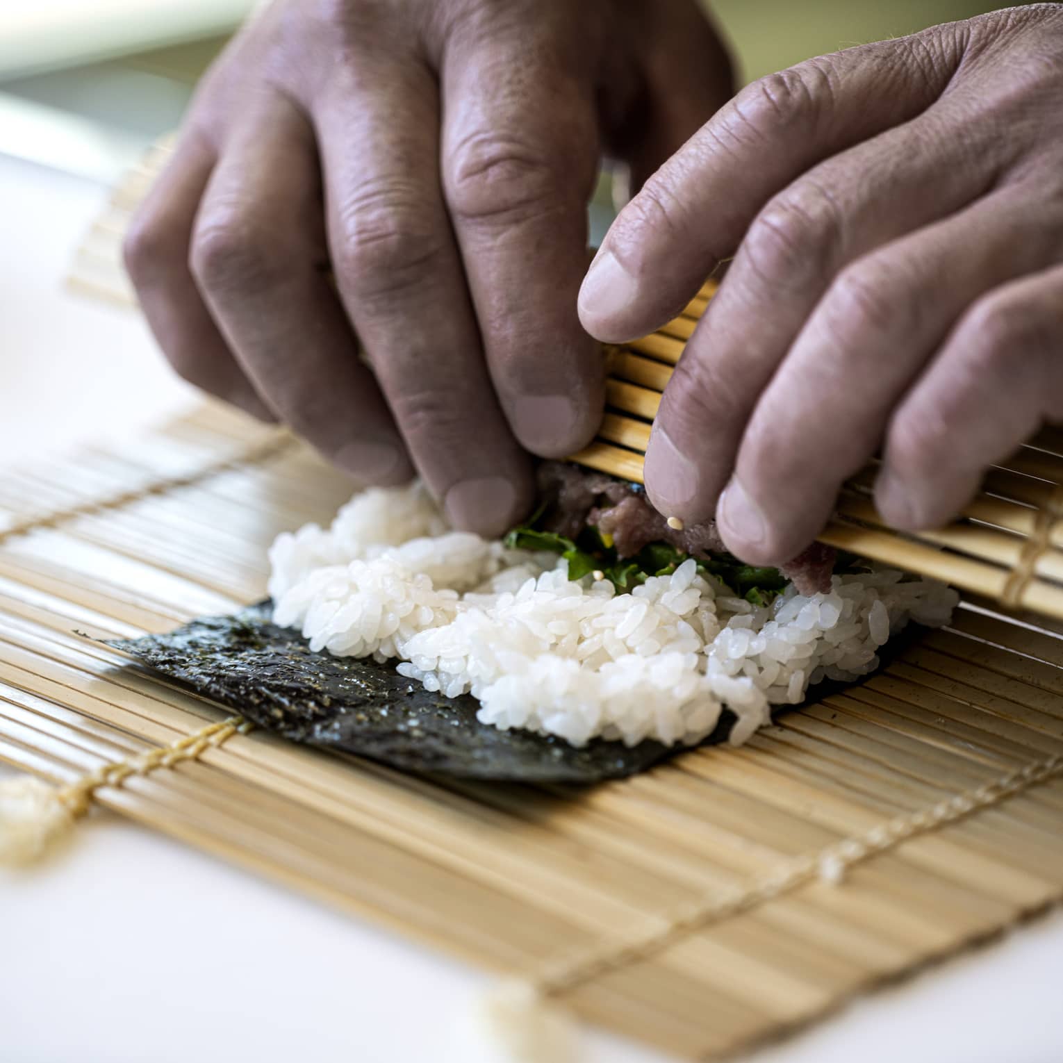 A four seasons chef rolls sushi with a bamboo mat 