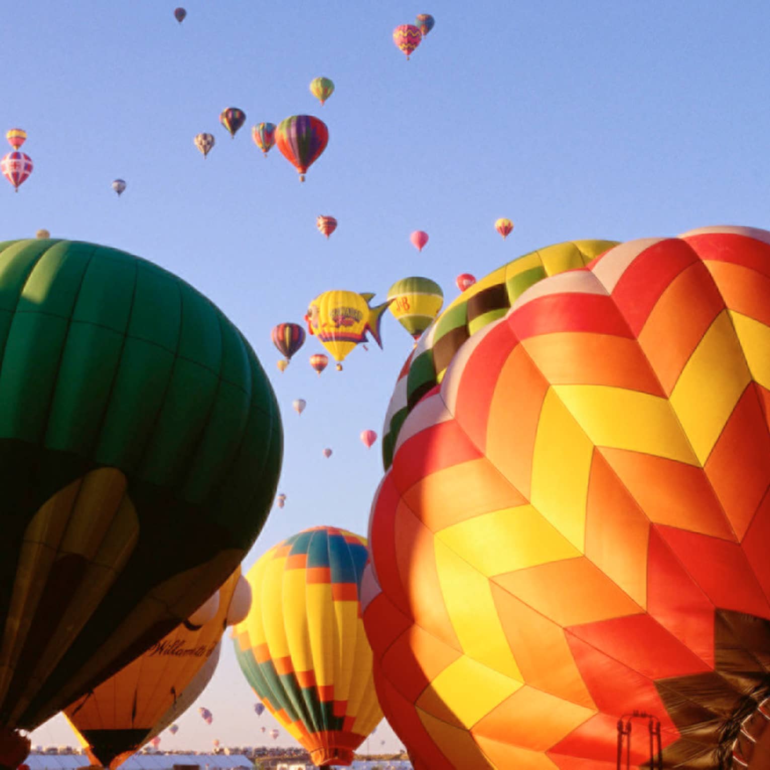 Clusters of colourful hot air balloons rising into blue sky