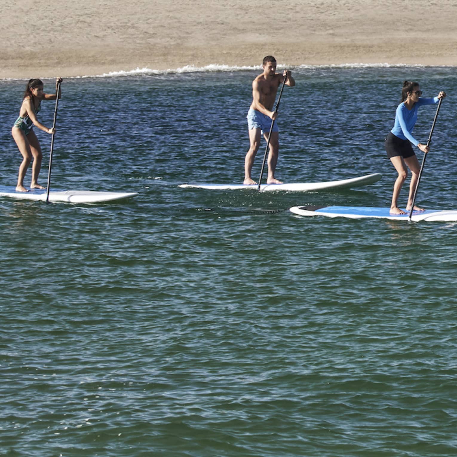 Three people on paddle boards in the water with a hotel behind them.