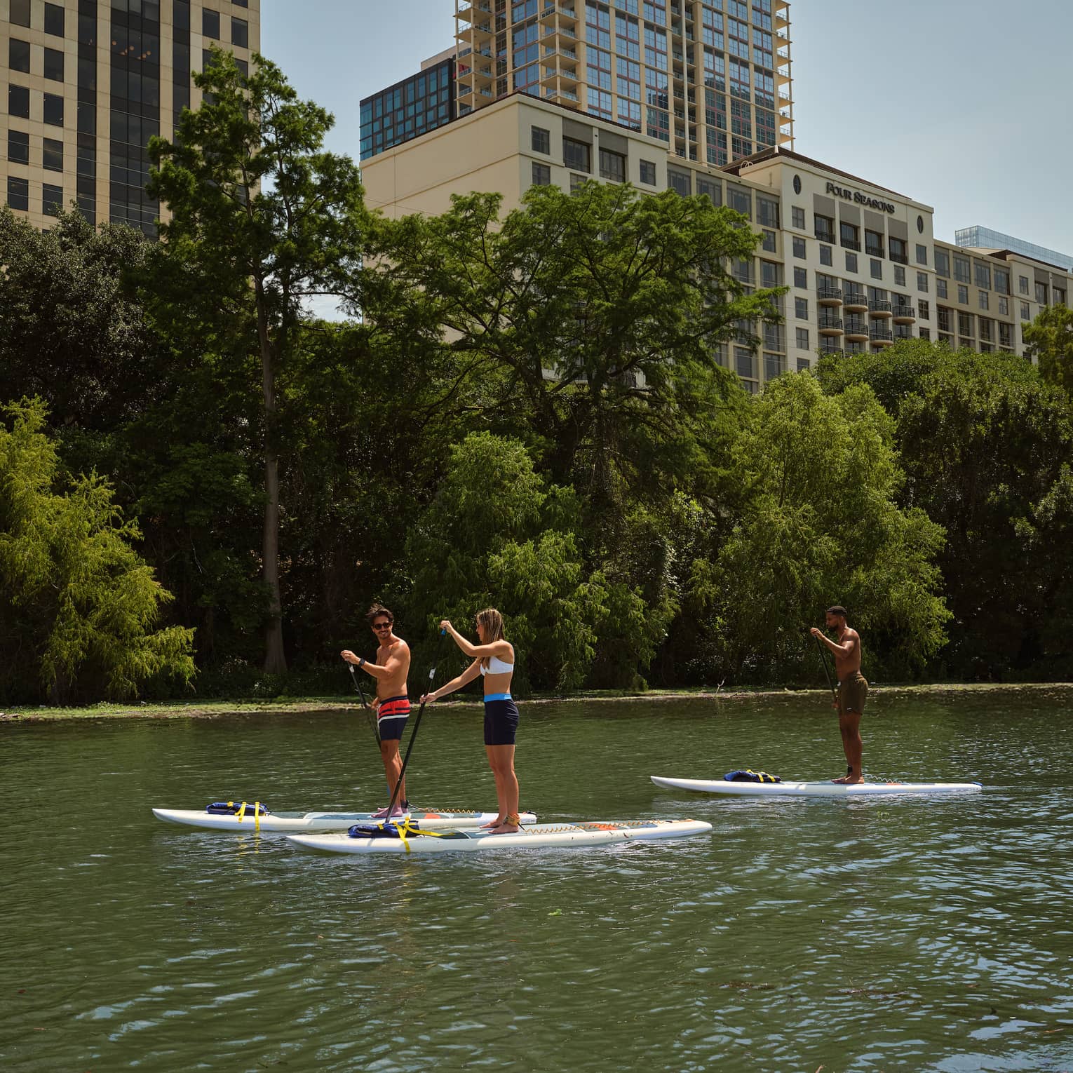 Guests on a stand-up paddleboard in the water with buildings in the background