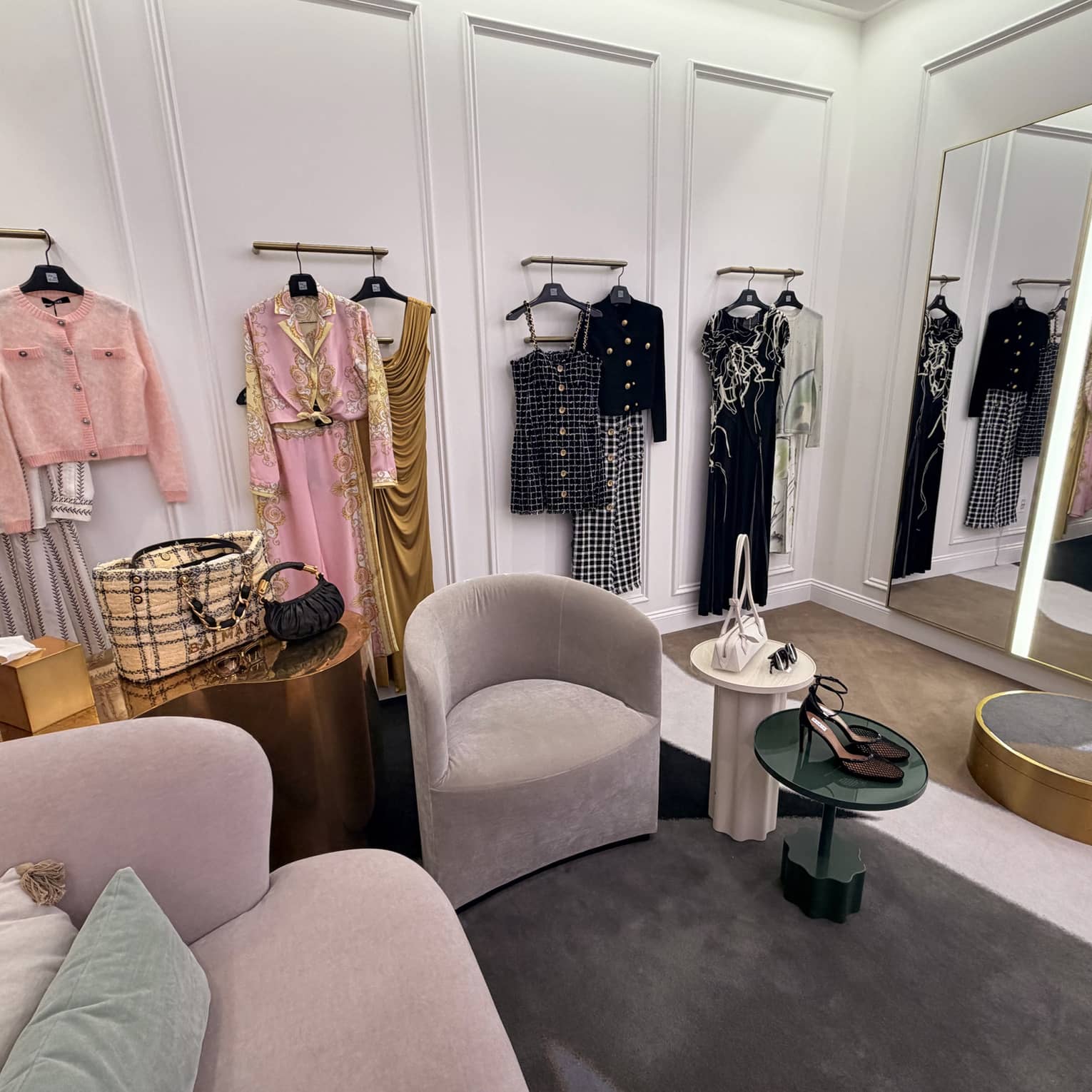 Large dressing room with arm chairs and tables and various curated outfts hung on the wall