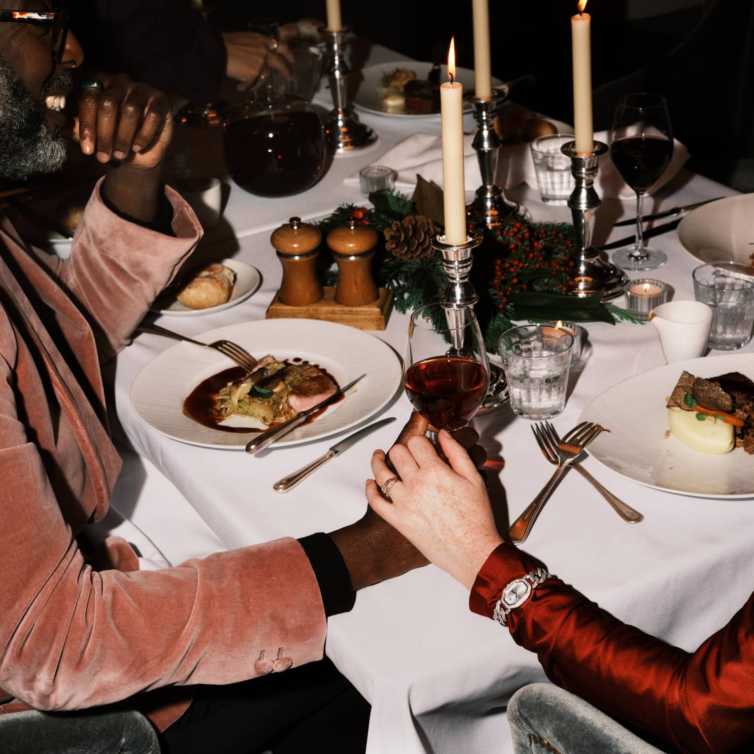 Two guests sitting at a dining table holding hands and a glass of wine.