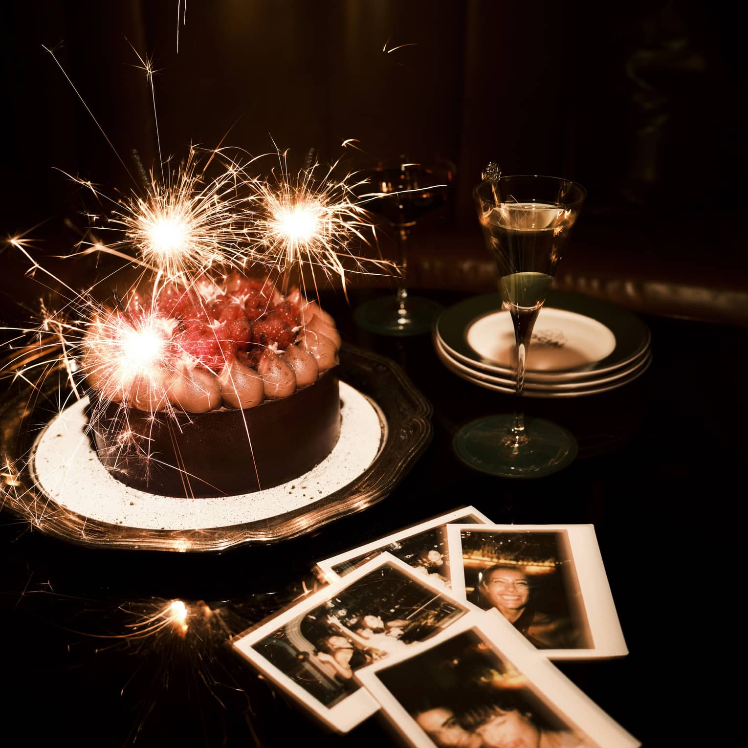 Sparkler candles in a chocolate cake and polaroid pictures nearby on a table