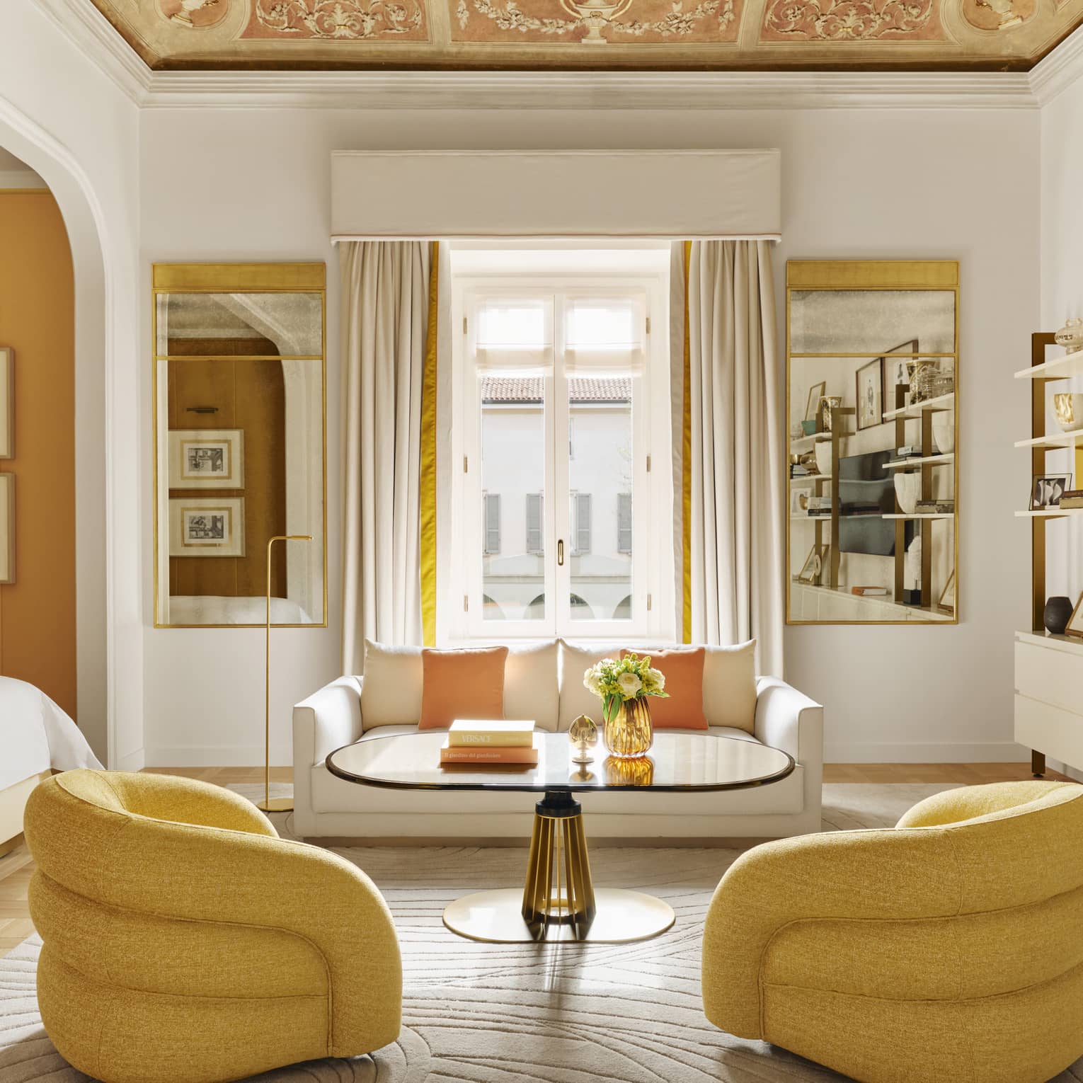 Luxury hotel suite with frescoed ceiling and modern yellow arm chairs, white sofa and adjacent bedroom