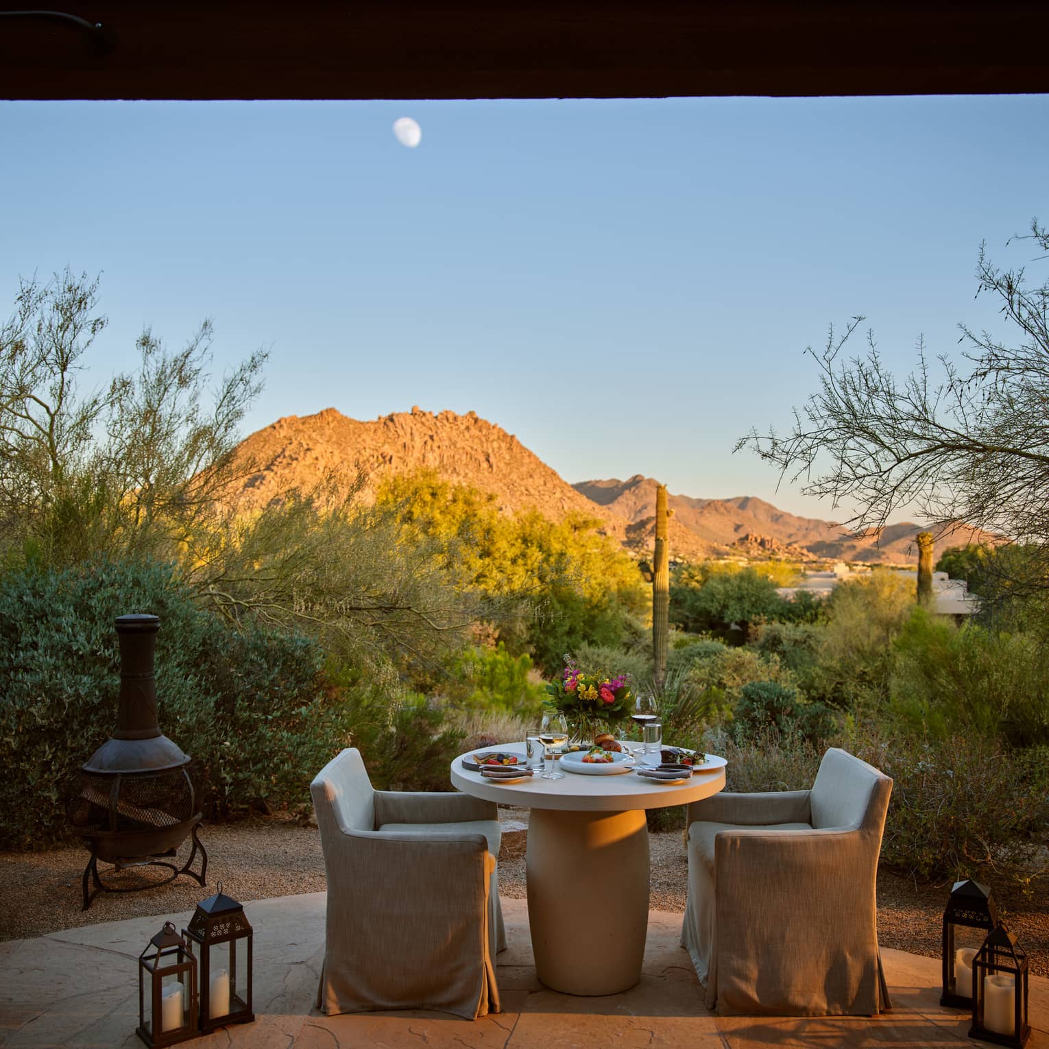 Two chairs and a table outside with lanterns and a view of the mountains.