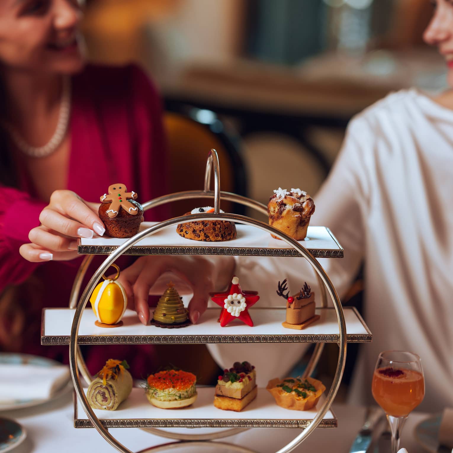 Two guests reach for pastries served on a three-tiered silver tray