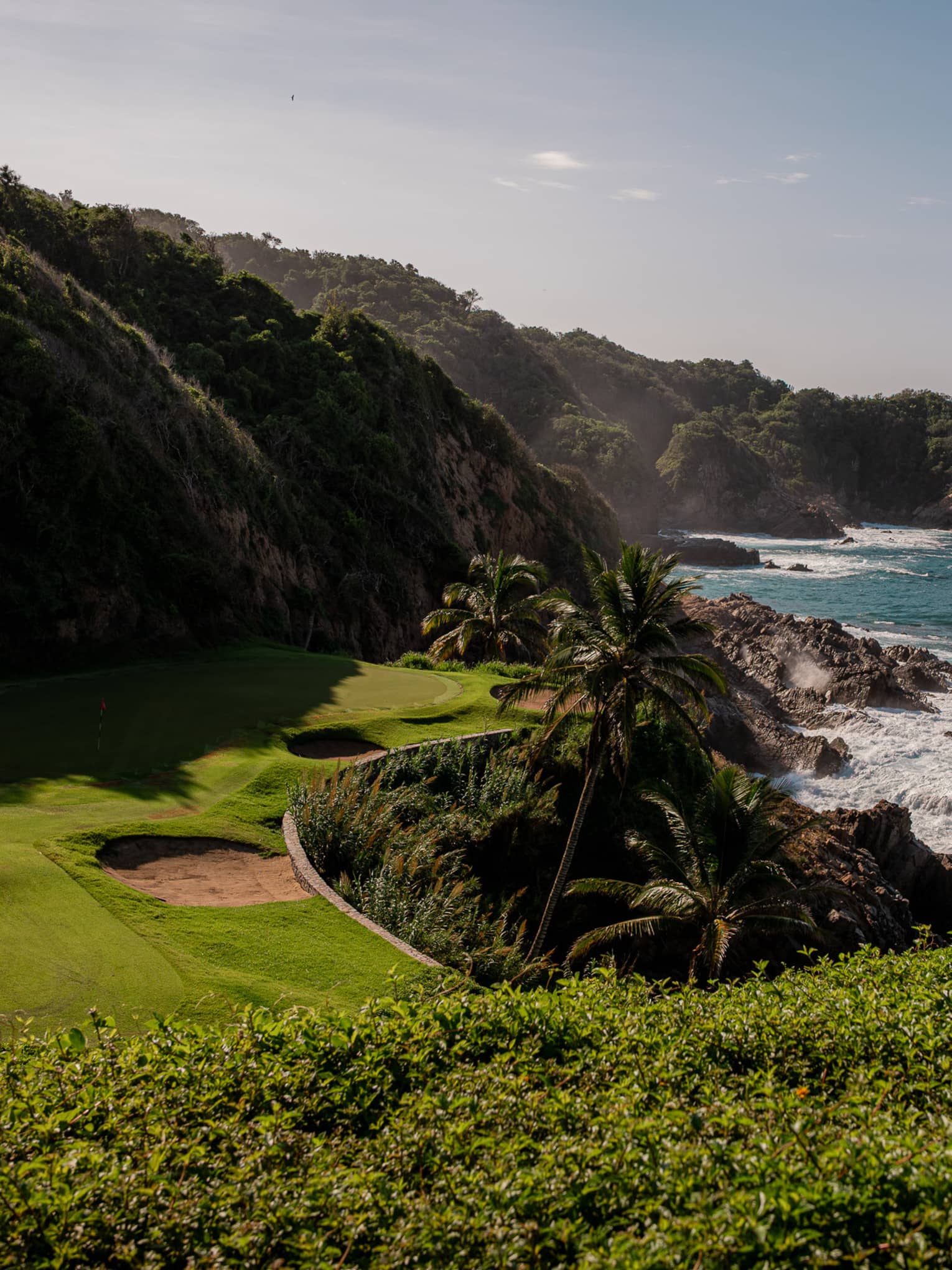 A golf course green nestled between hills and the sea