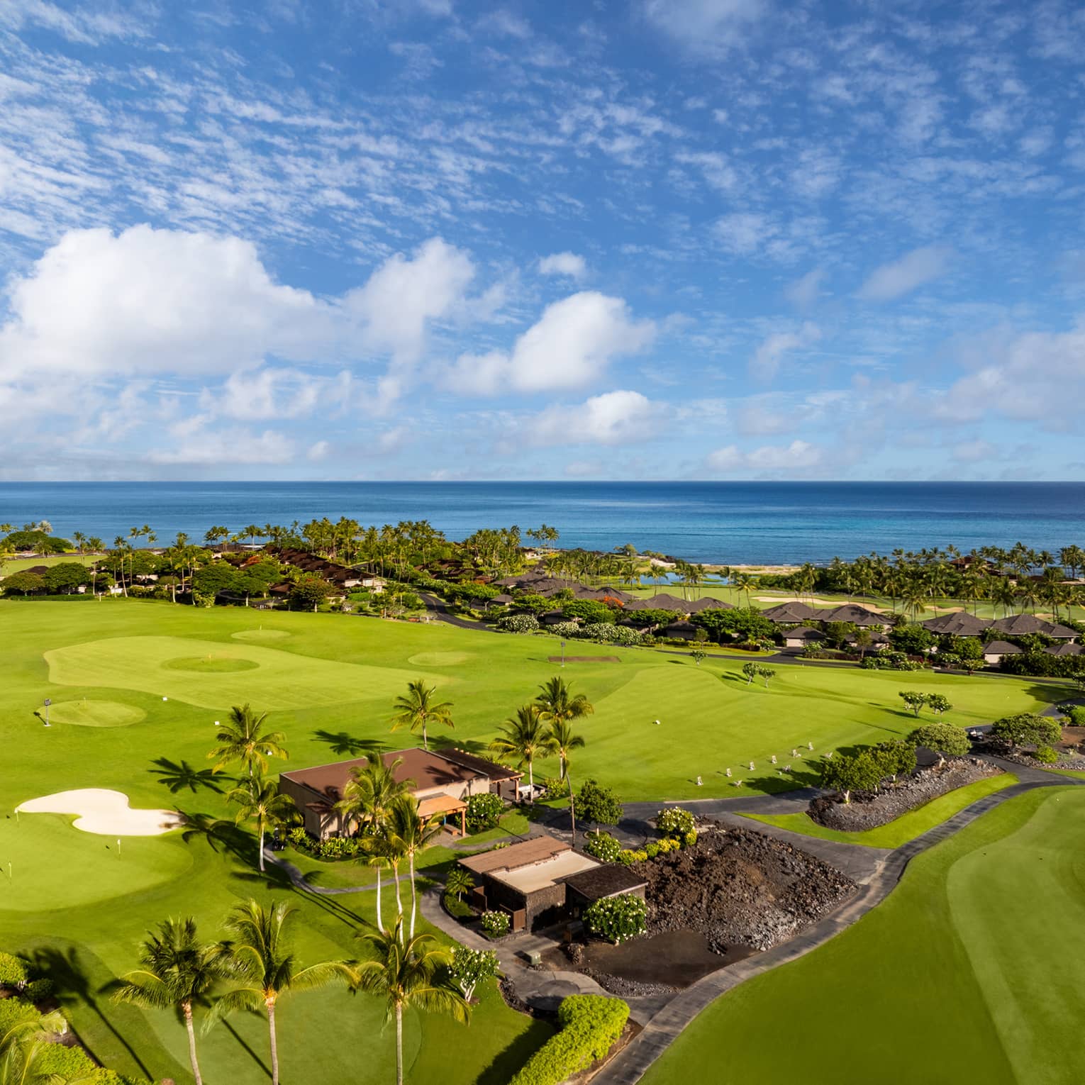 Aeriel view of a lush green golf course with natural lava formations and the ocean in the background.