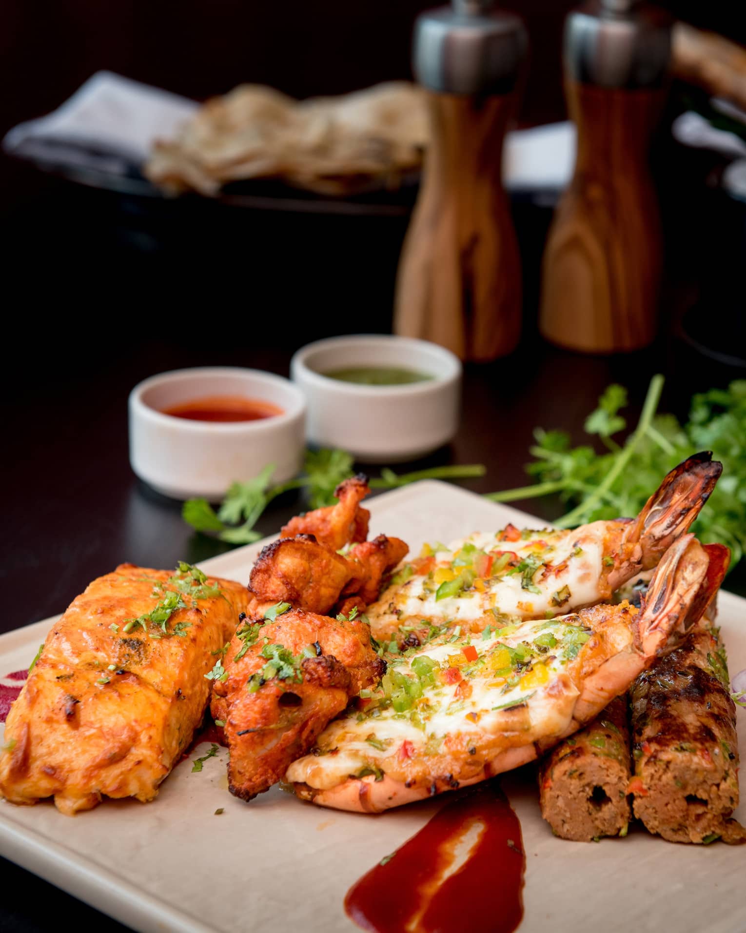 Seafood and meat kebabs garnished with fresh herbs on white platter