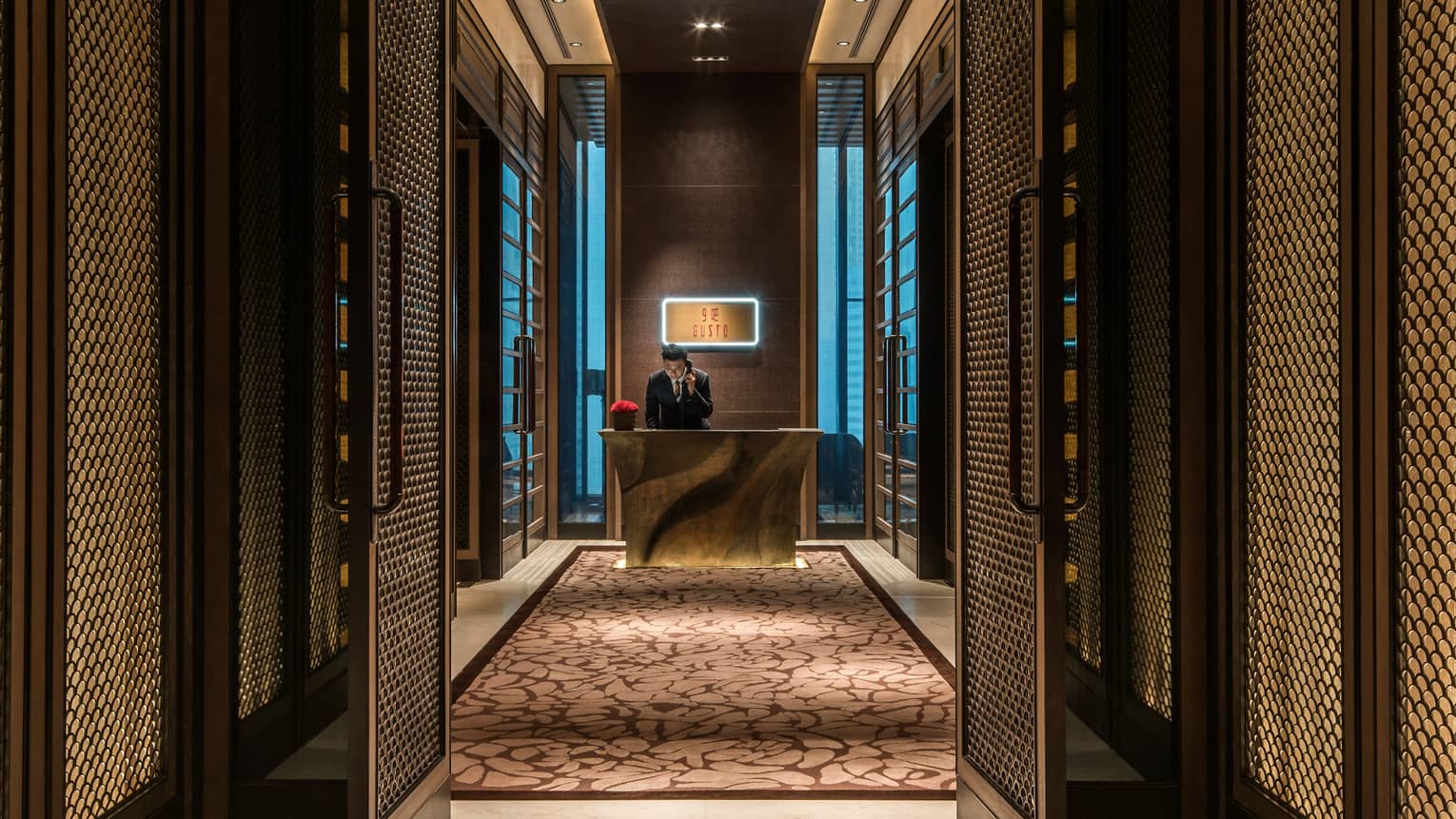 Gusto host on phone at gold desk past tall doors with decorative screens