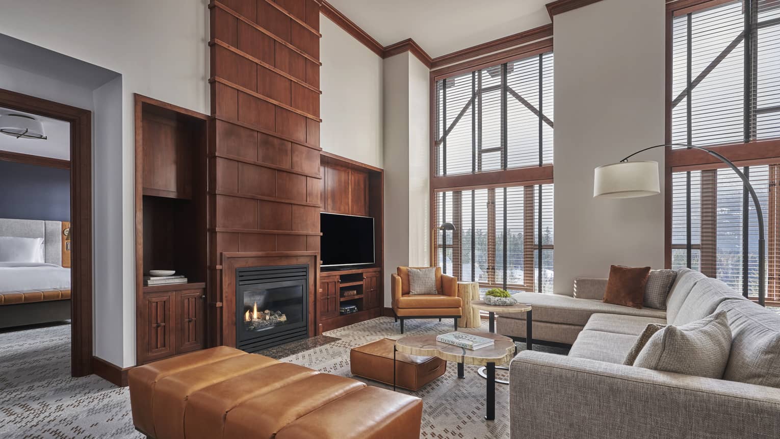 The Summit Suite at Four Seasons Whistler, featuring a luxurious and open interior with high ceilings and large, floor-to-ceiling windows that provide ample natural light and stunning views. The suite includes a cozy living area with a gray sectional sofa, a sleek glass coffee table, and a rich tan leather ottoman. A modern fireplace is set into a brick wall, adding warmth to the space. The bedroom area is visible in the background.,The Summit Suite at Four Seasons Whistler, featuring a luxurious and open interior with high ceilings and large, floor-to-ceiling windows that provide ample natural light and stunning views. The suite includes a cozy living area with a gray sectional sofa, a sleek glass coffee table, and a rich tan leather ottoman. A modern fireplace is set into a brick wall, adding warmth to the space. The bedroom area is visible in the background.
