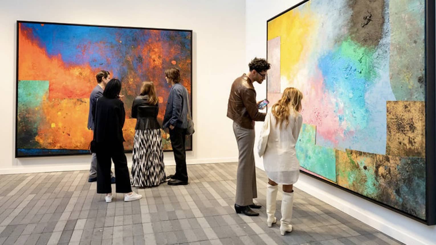 People observing large paintings at an art gallery
