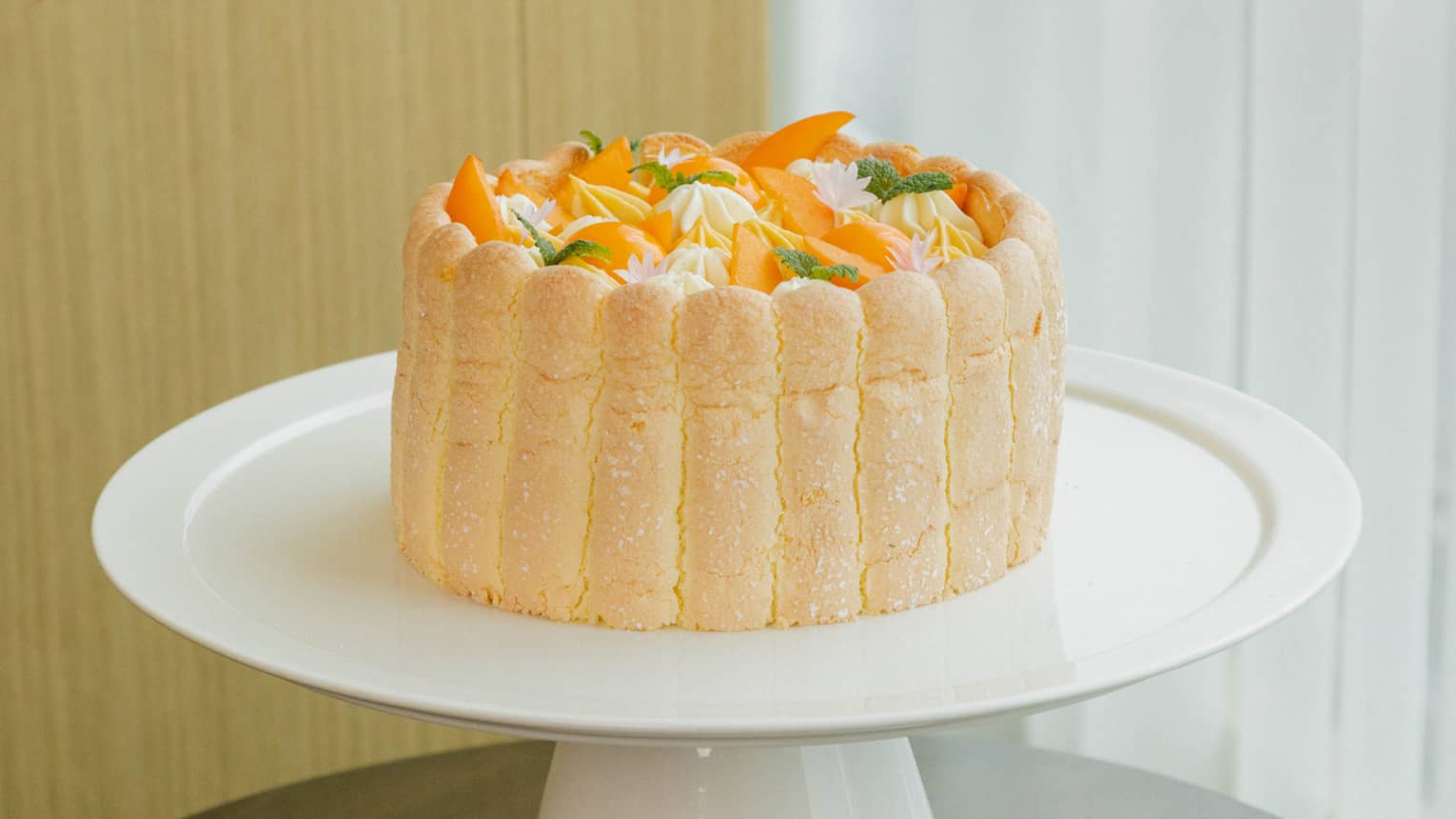 Round cake made with apricot Diplomate, ladyfinger sponge and apricot compote sits atop a round white cake stand