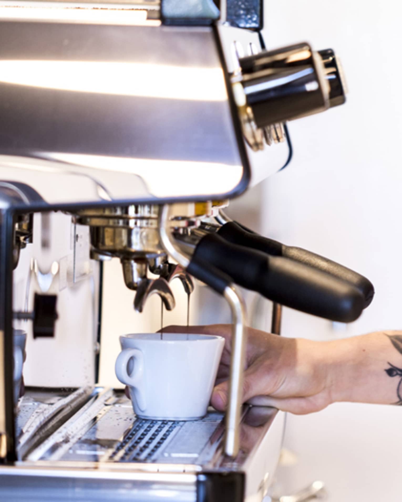 Smiling barista with checked shirt, apron makes espresso at espresso machine 