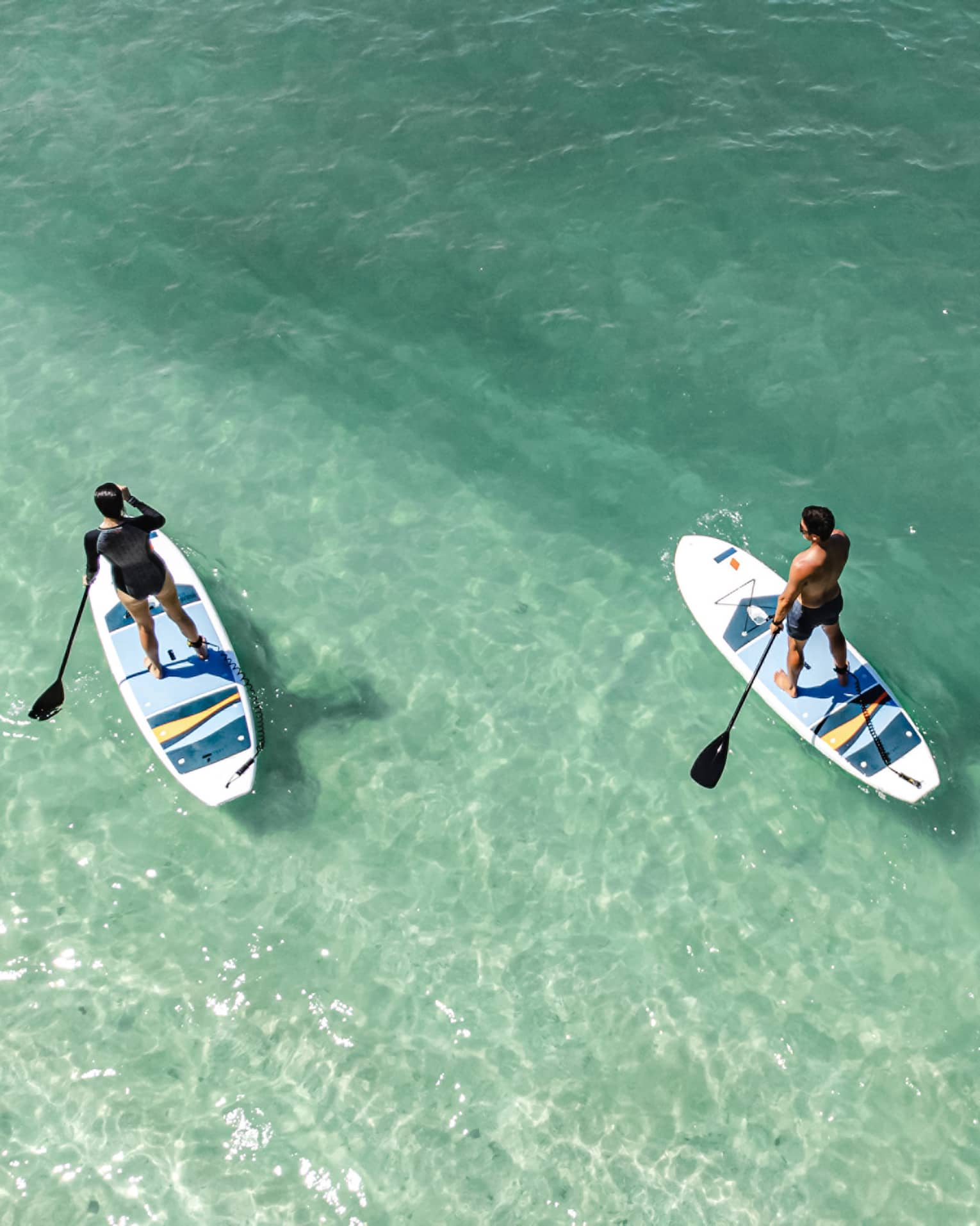 Aerial view of two people paddleboarding in clear green-blue water