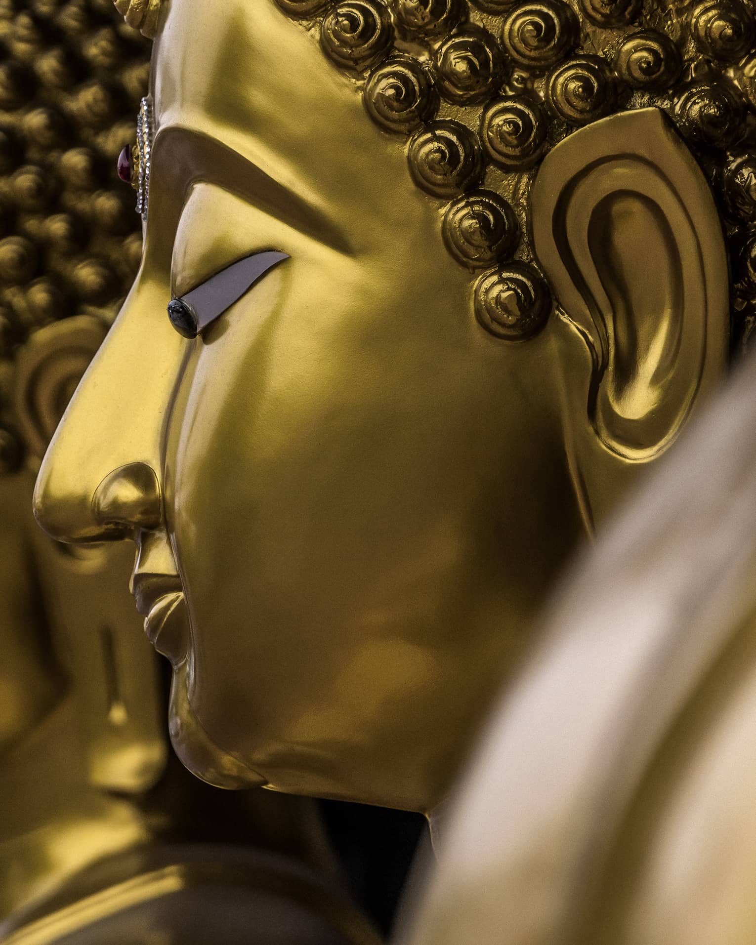 Two gold statues, side of women's face showing nose, ears, closed eyes and hair