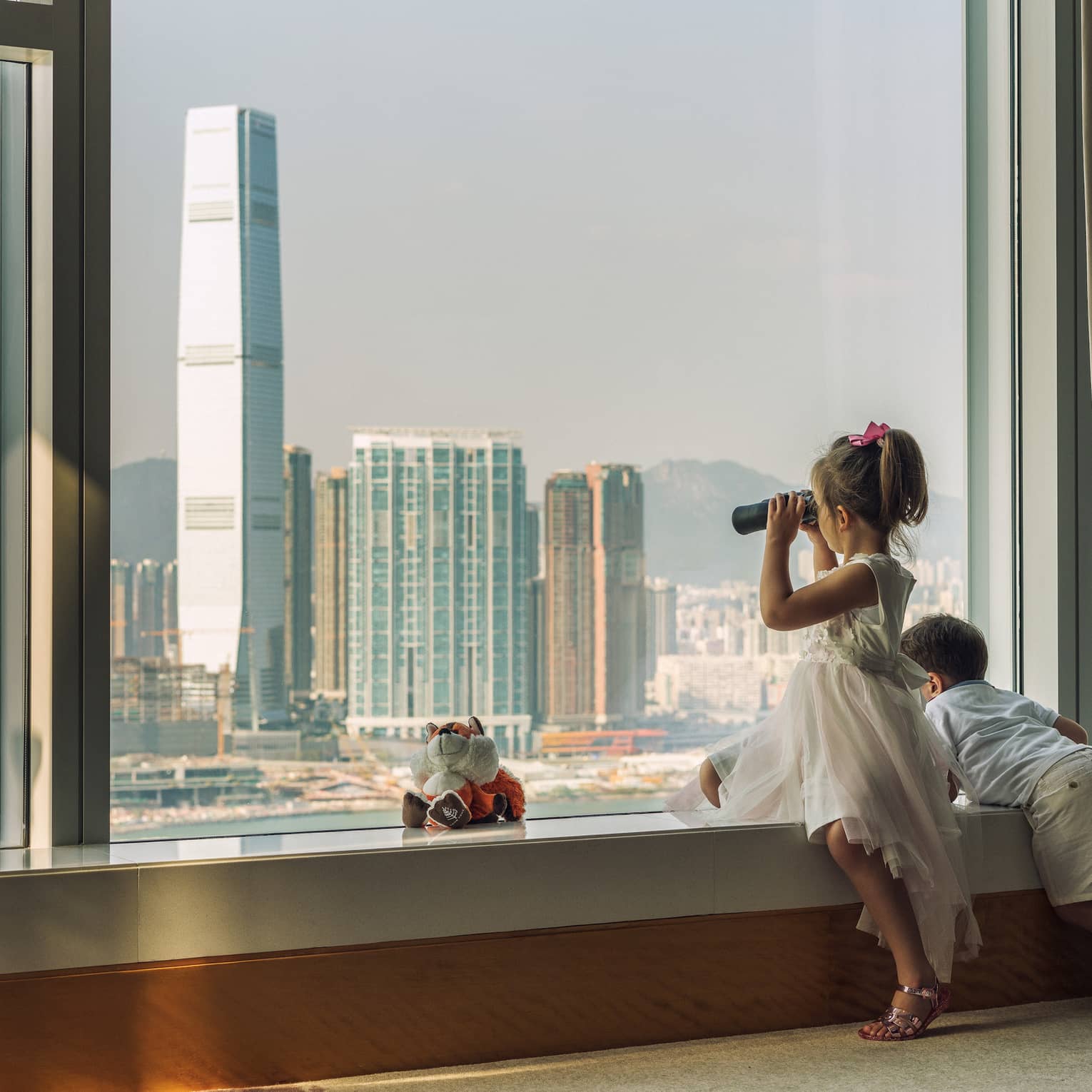 Young boy and girl looking out hotel window to Hong Kong cityscape