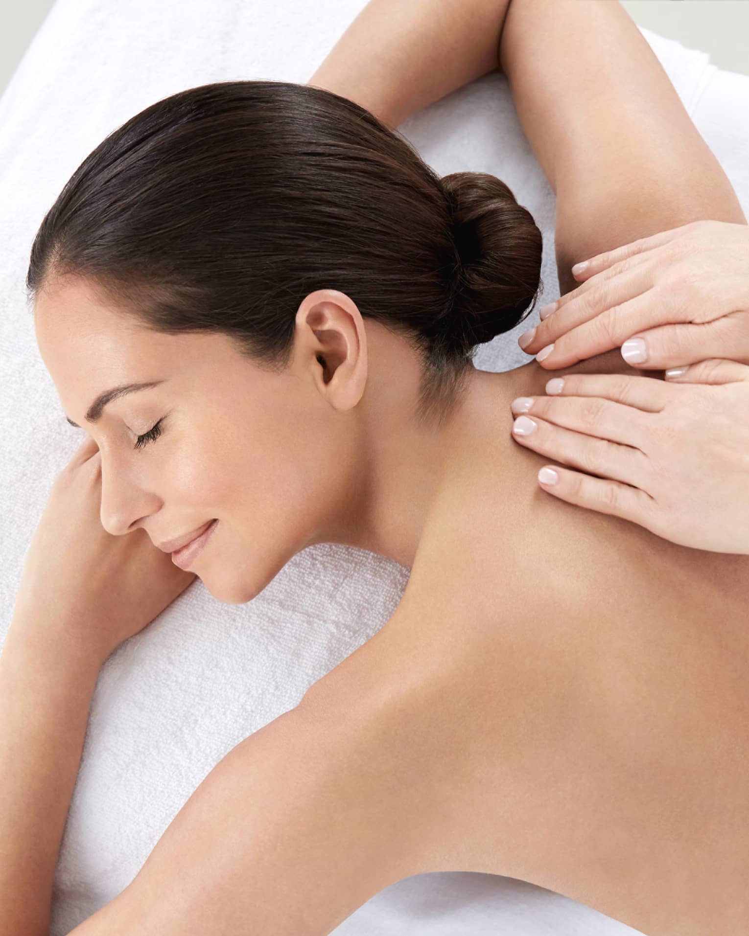 Woman smiles, lies on massage table as hands massage bare shoulders
