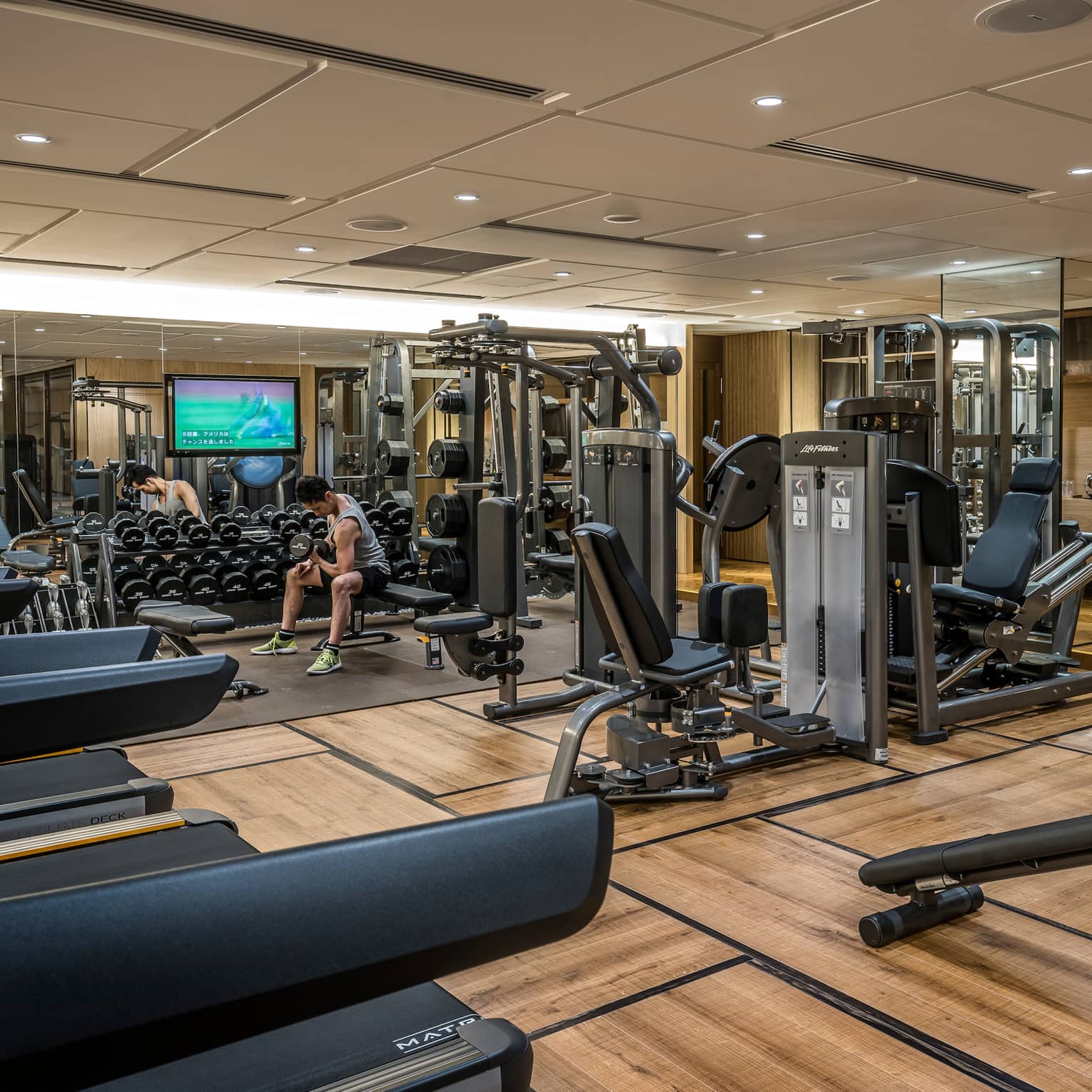 Man sits on bench, lifts weights on Fitness Centre by cardio machines 