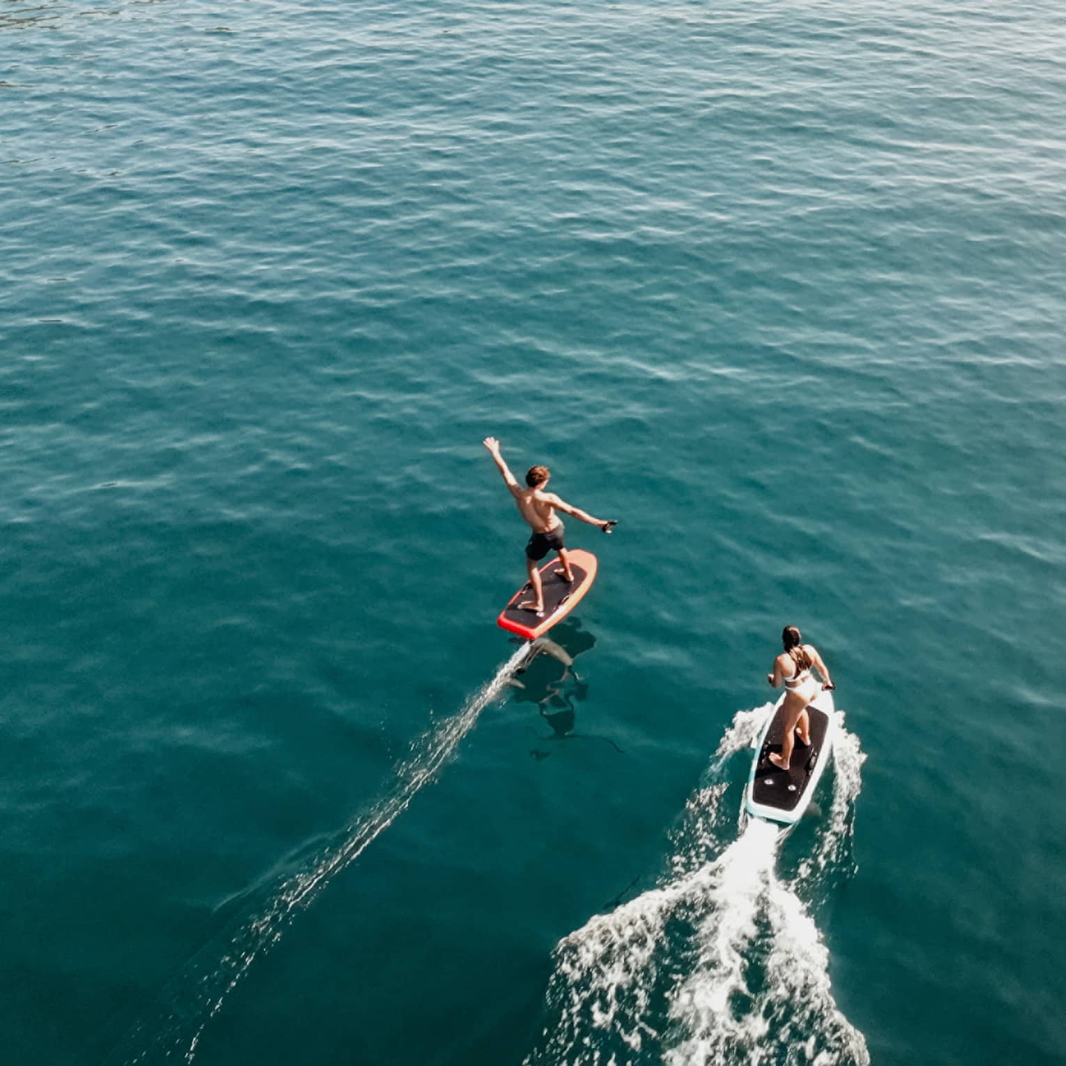 Aerial view of two people riding e0foil surfboards on blue-green water
