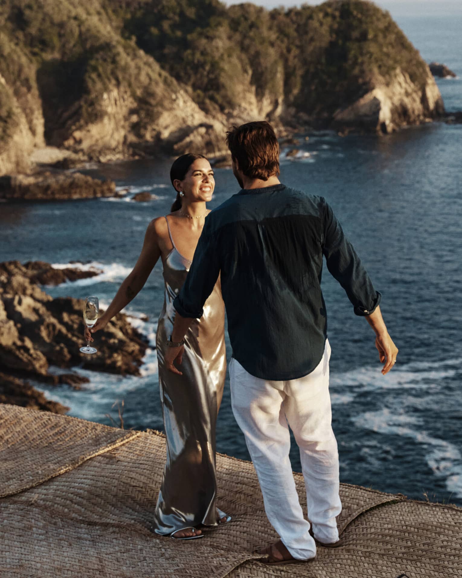 A couple standing near a vast, shimmering ocean against a backdrop of majestic cliffs, embraced by the beauty of nature