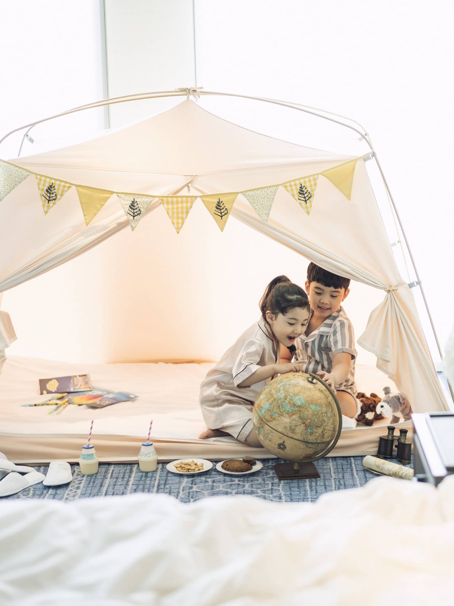 Two smiling children sit in a white play tent in a guest room at Four Seasons Hotel Seoul, with toys and snacks around them