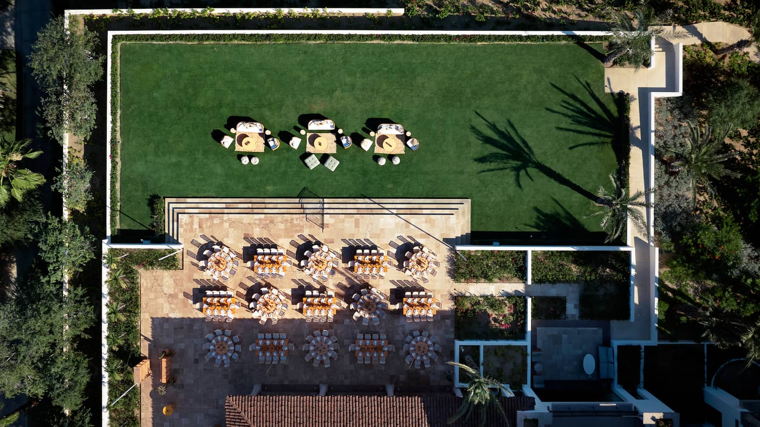 Bird's-eye view of a large lawn surrounded by trees, with tables placed and set for an event