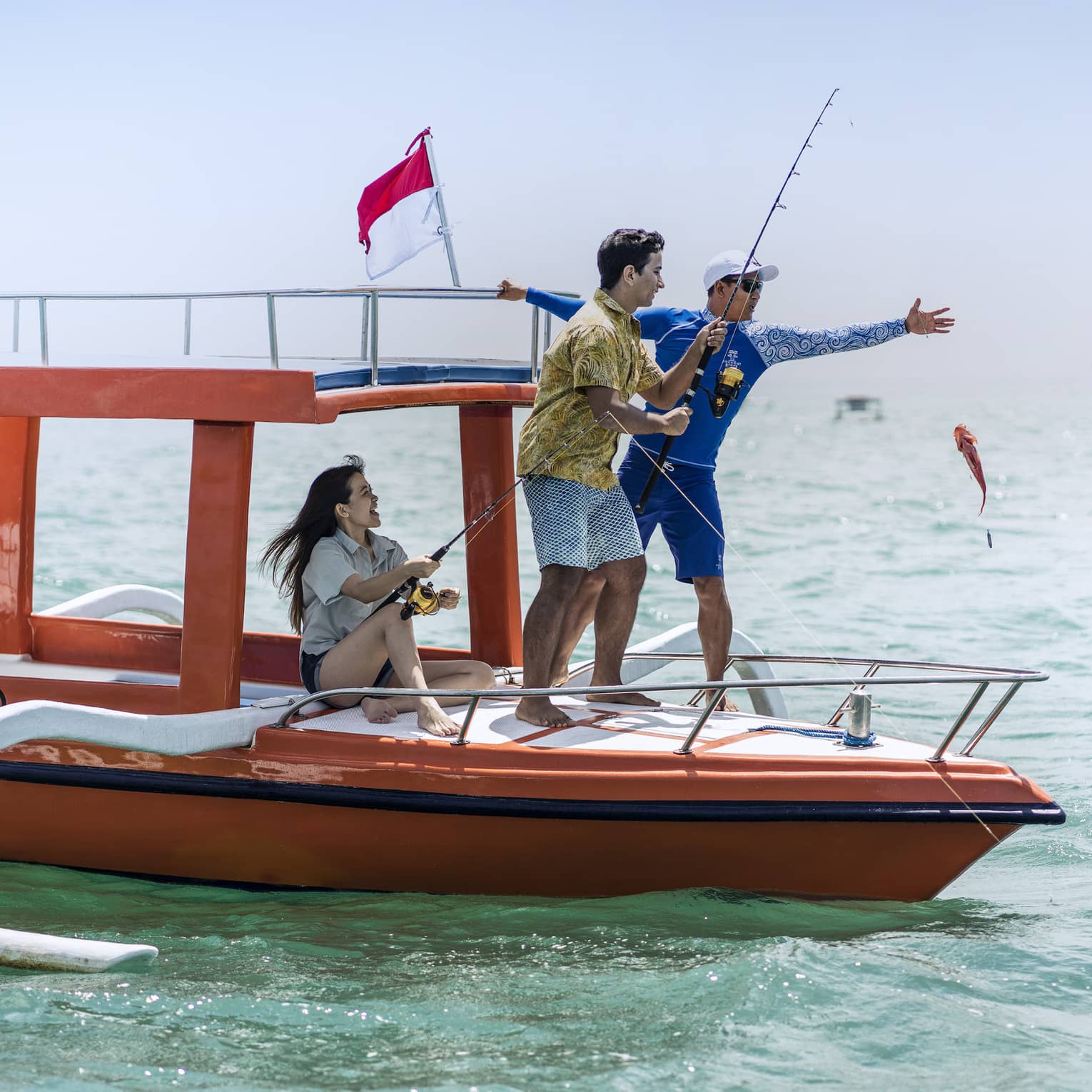 Tour guide teaches two guests to fish on a traditional jukung fishing boat on the open ocean