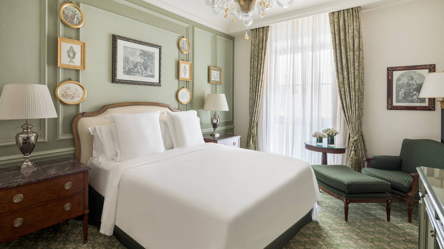 Bedroom with light green walls, small picture frames, crystal chandelier, white king bed