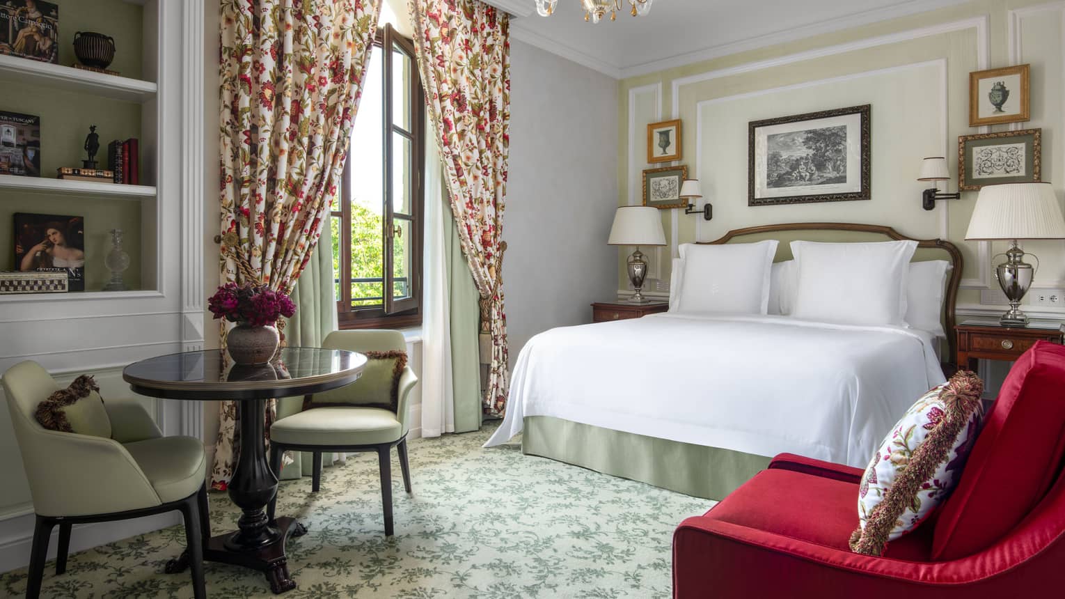 Hotel suite bedroom with king bed, red arm chair, small table and two chairs, and floral drapery, at Four Seasons Hotel Florence