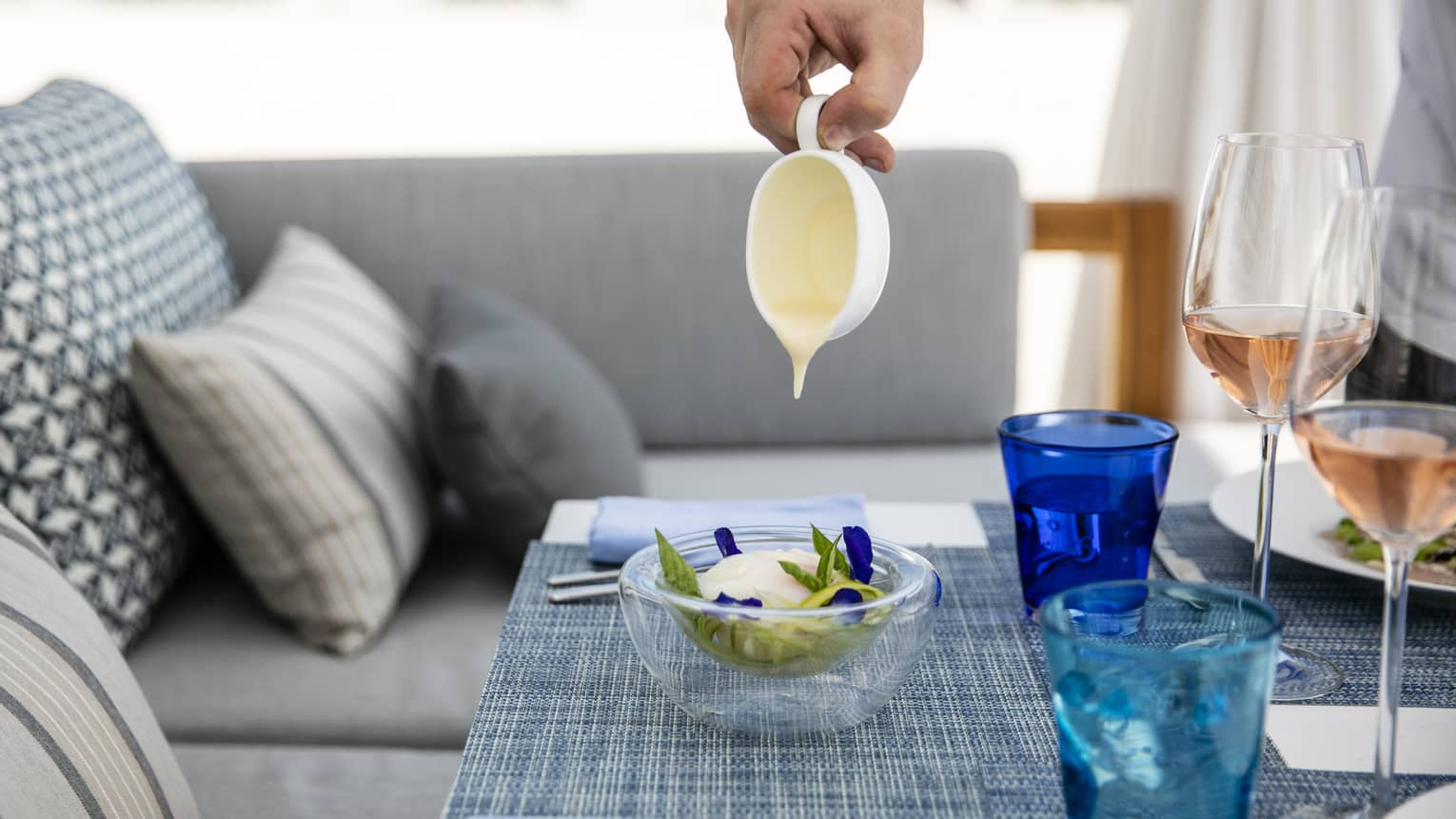 A person pouring some kind of glaze over a dish on a tastefully set table overlooking the ocean in Four Seasons Maldives - Landaa