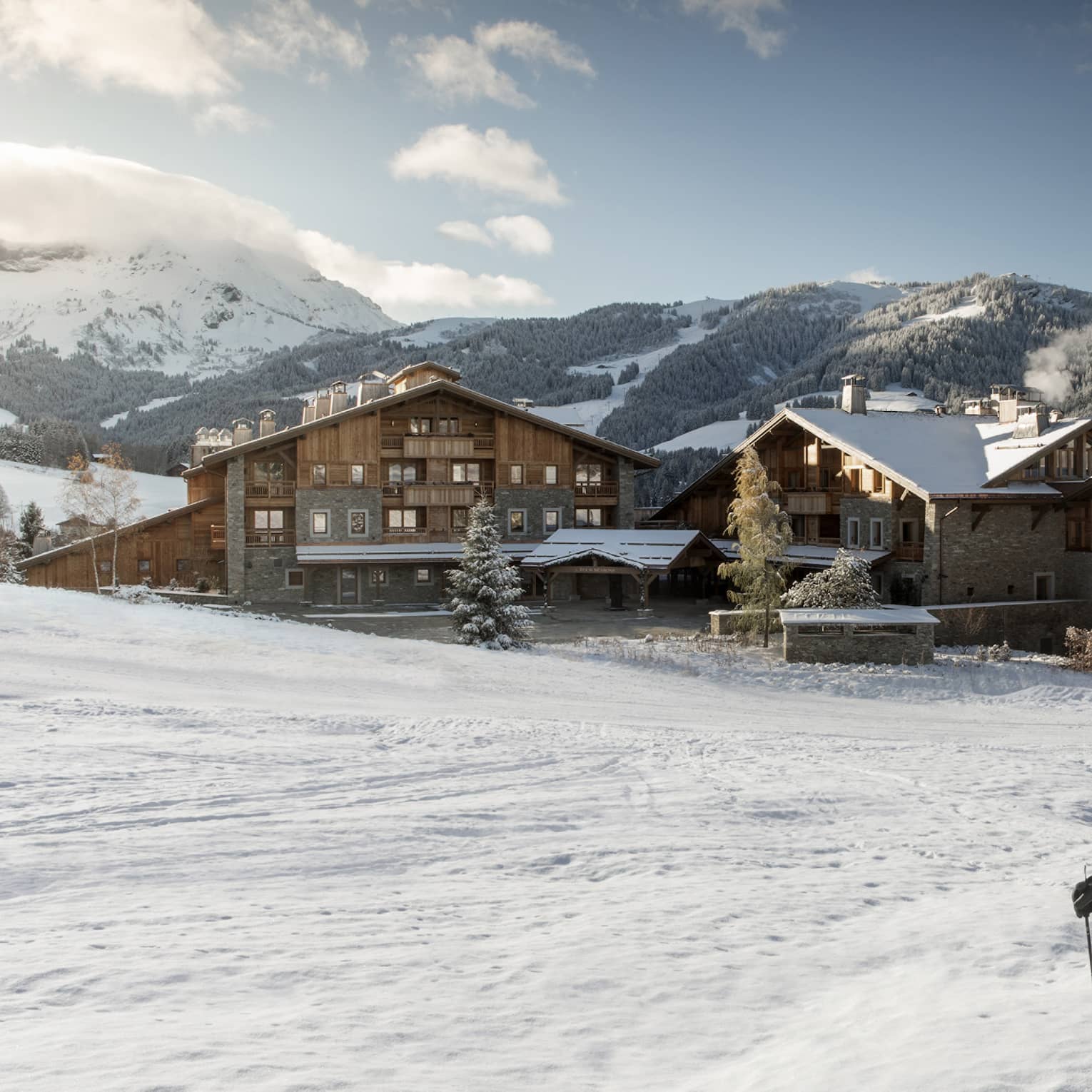 Man, woman on skis at top of snowy hill, Four Seasons Hotel Megeve in background