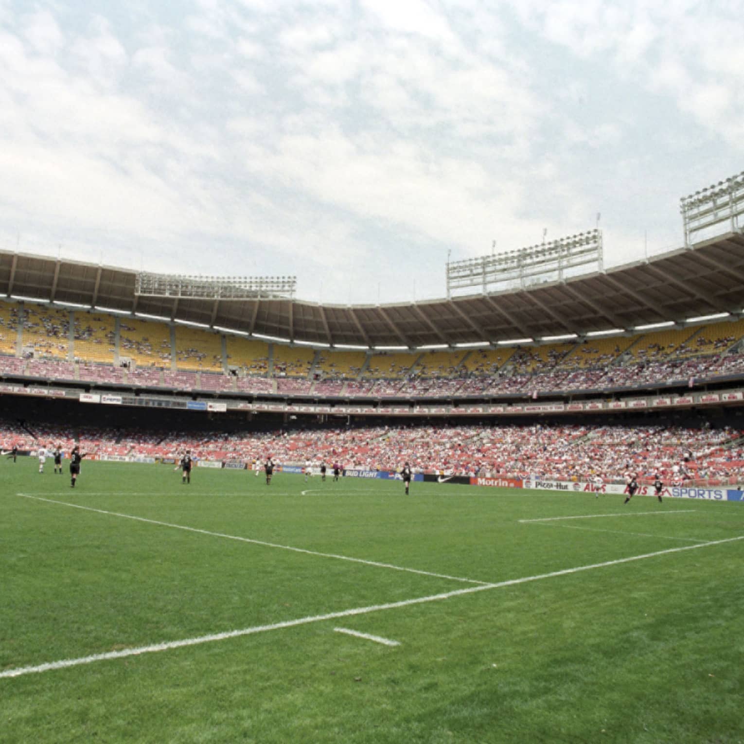 View across soccer field with players below crowds in stadium stands 