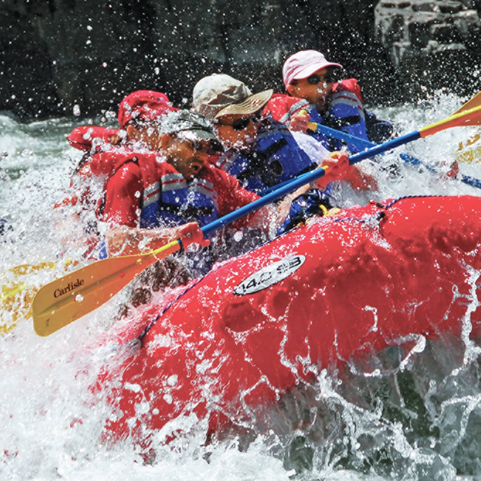 Water sprays around red inflatable raft, people with paddles, life vests white water rafting