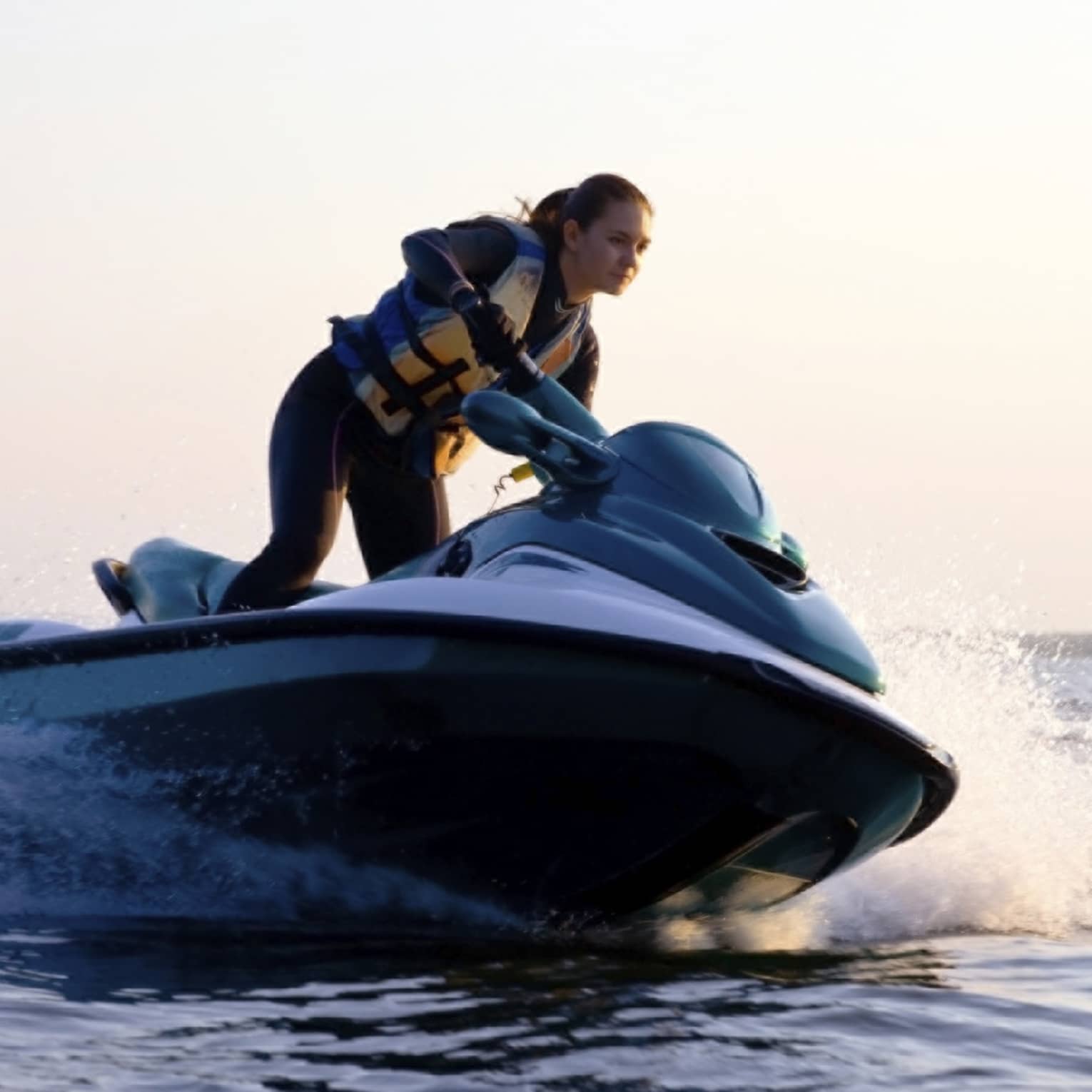 Woman wearing life jacket stands, steers jet ski on ocean at sunset