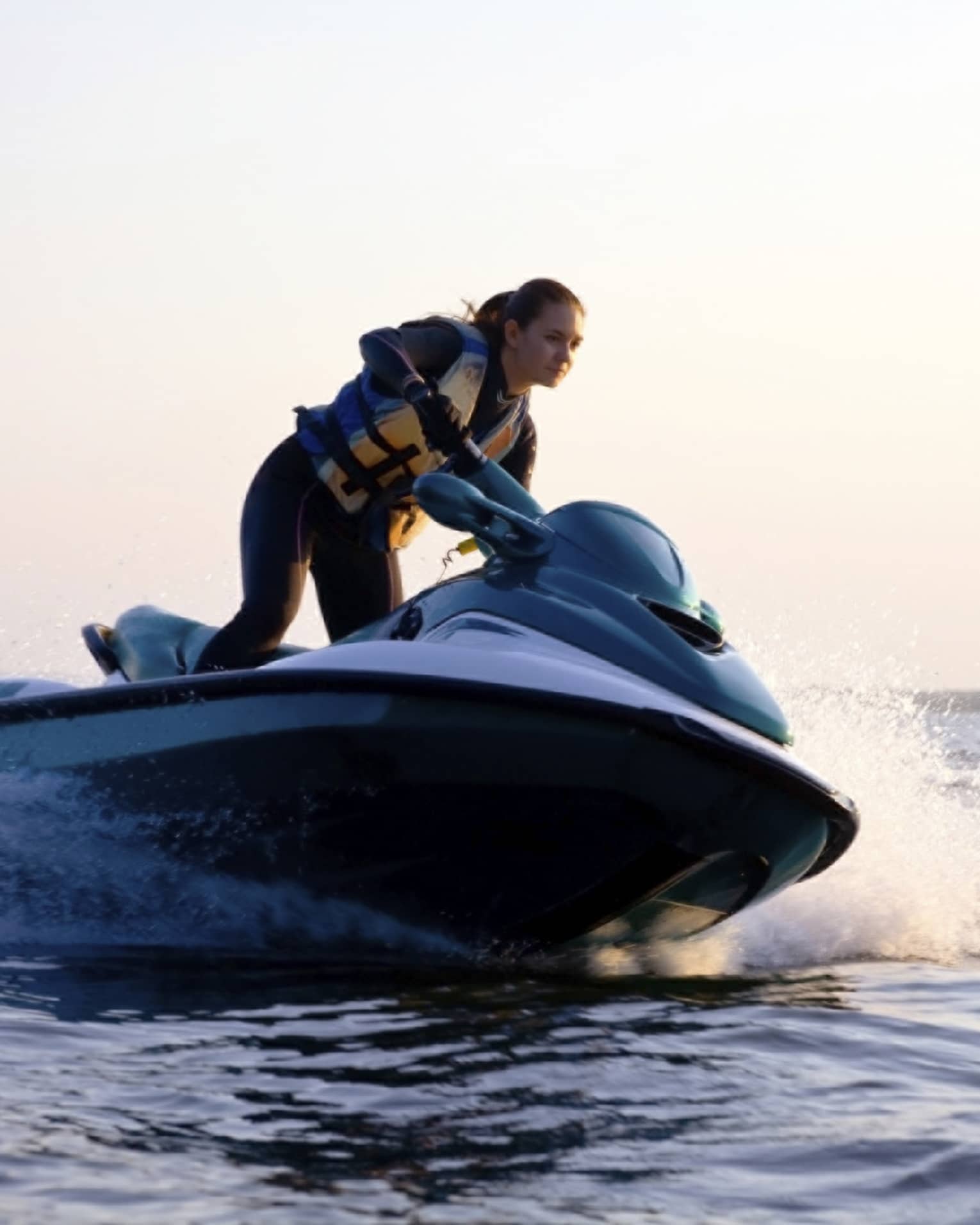 Woman wearing life jacket stands, steers jet ski on ocean at sunset