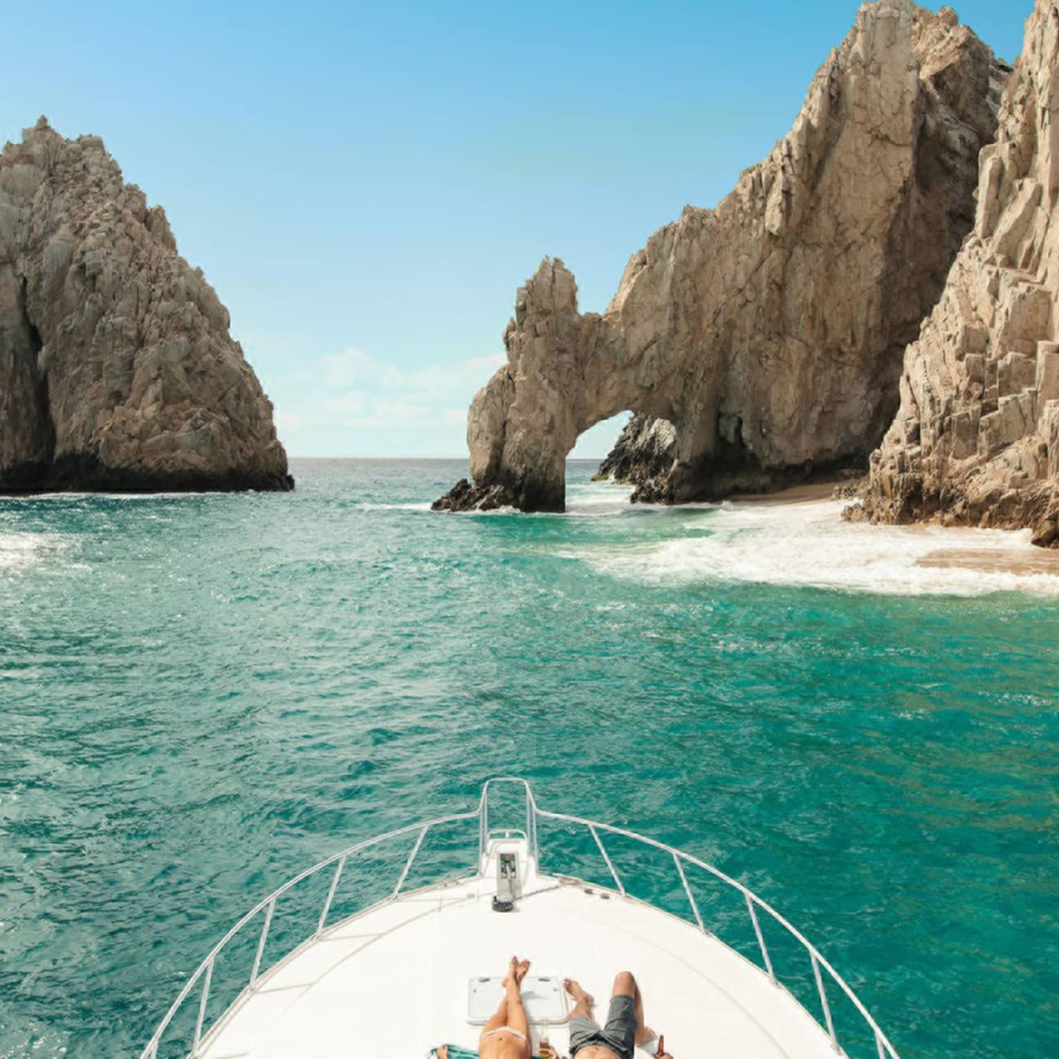 Two people lie on the front of a boat in Cabo