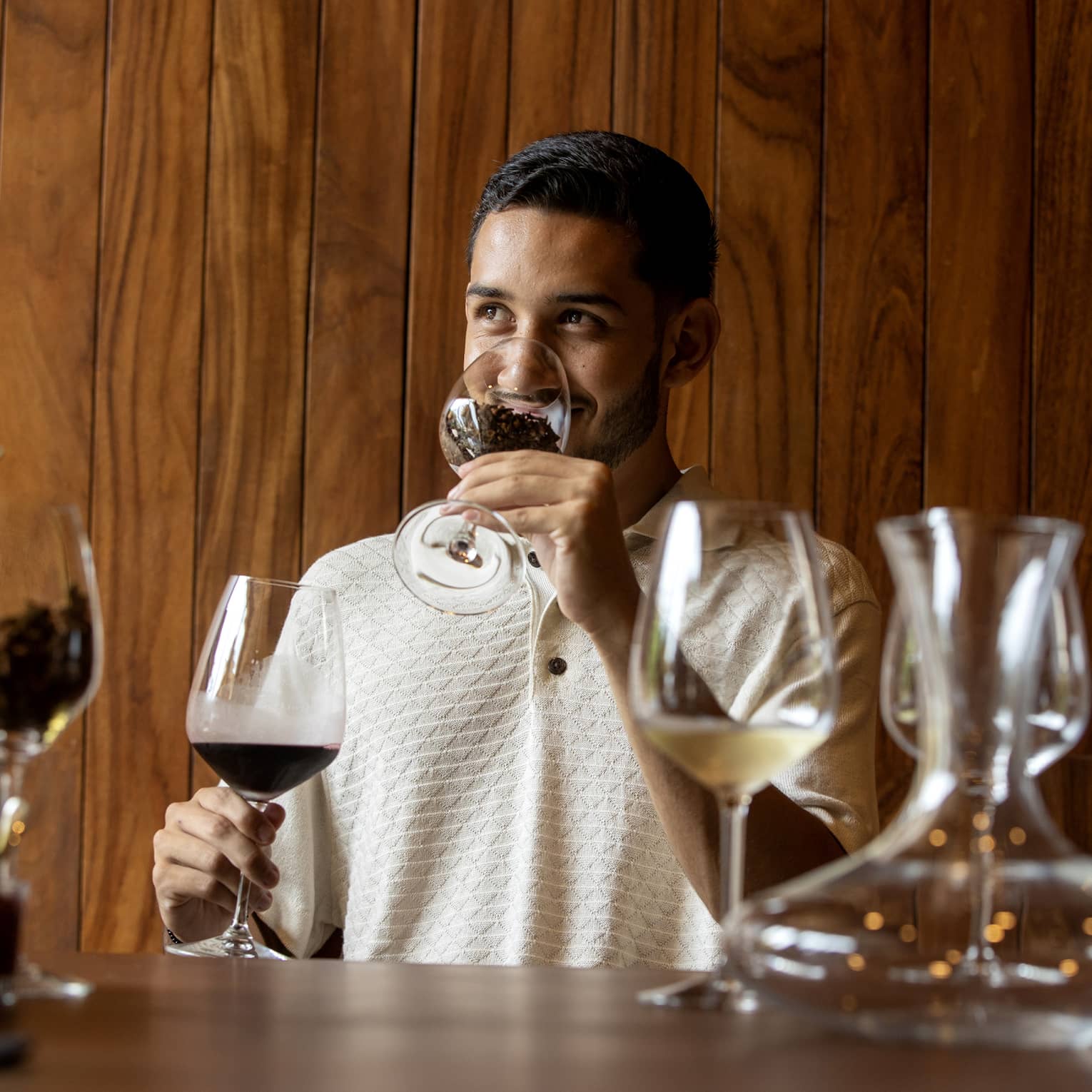 At a wine tasting, a guest smells coffee beans in a glass before tasting the glass of dark red wine held in his other hand. 