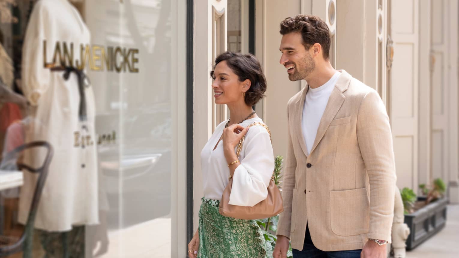 Two people smiling while window shopping in front of a boutique store.