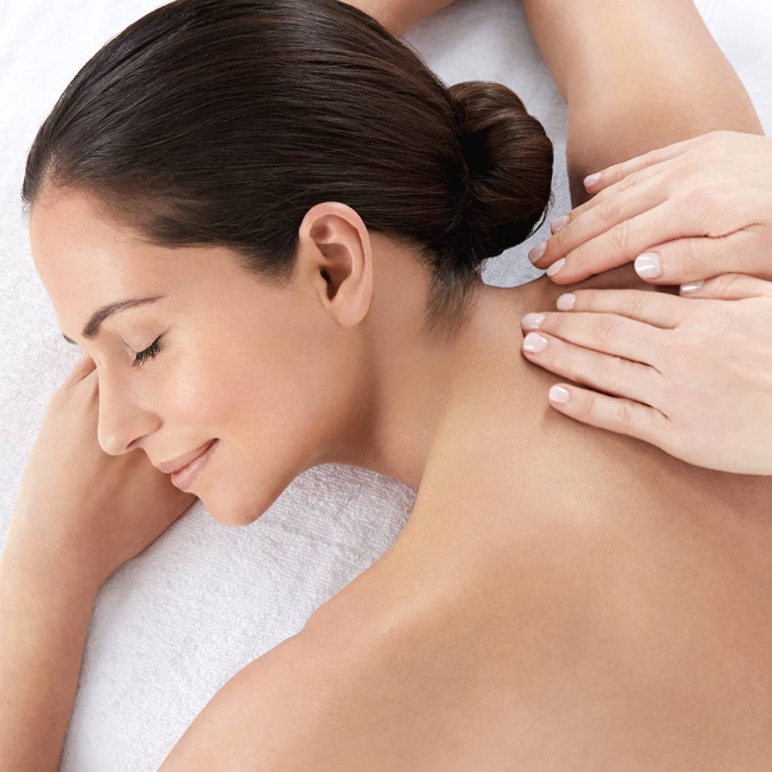 Woman smiles, lies on massage table as hands massage bare shoulders