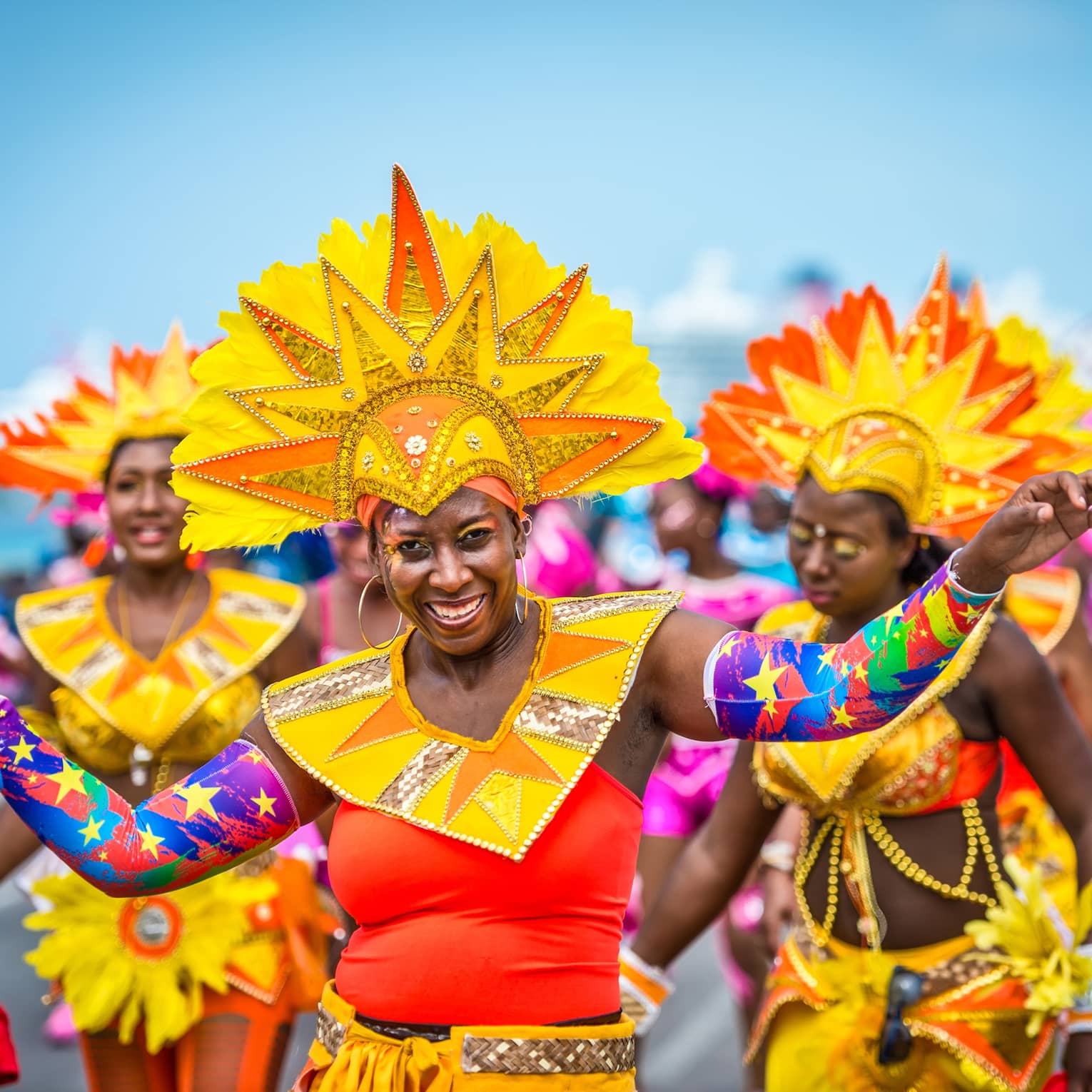 Women in brightly colored outfits with headdresses and arm bands smile and dance
